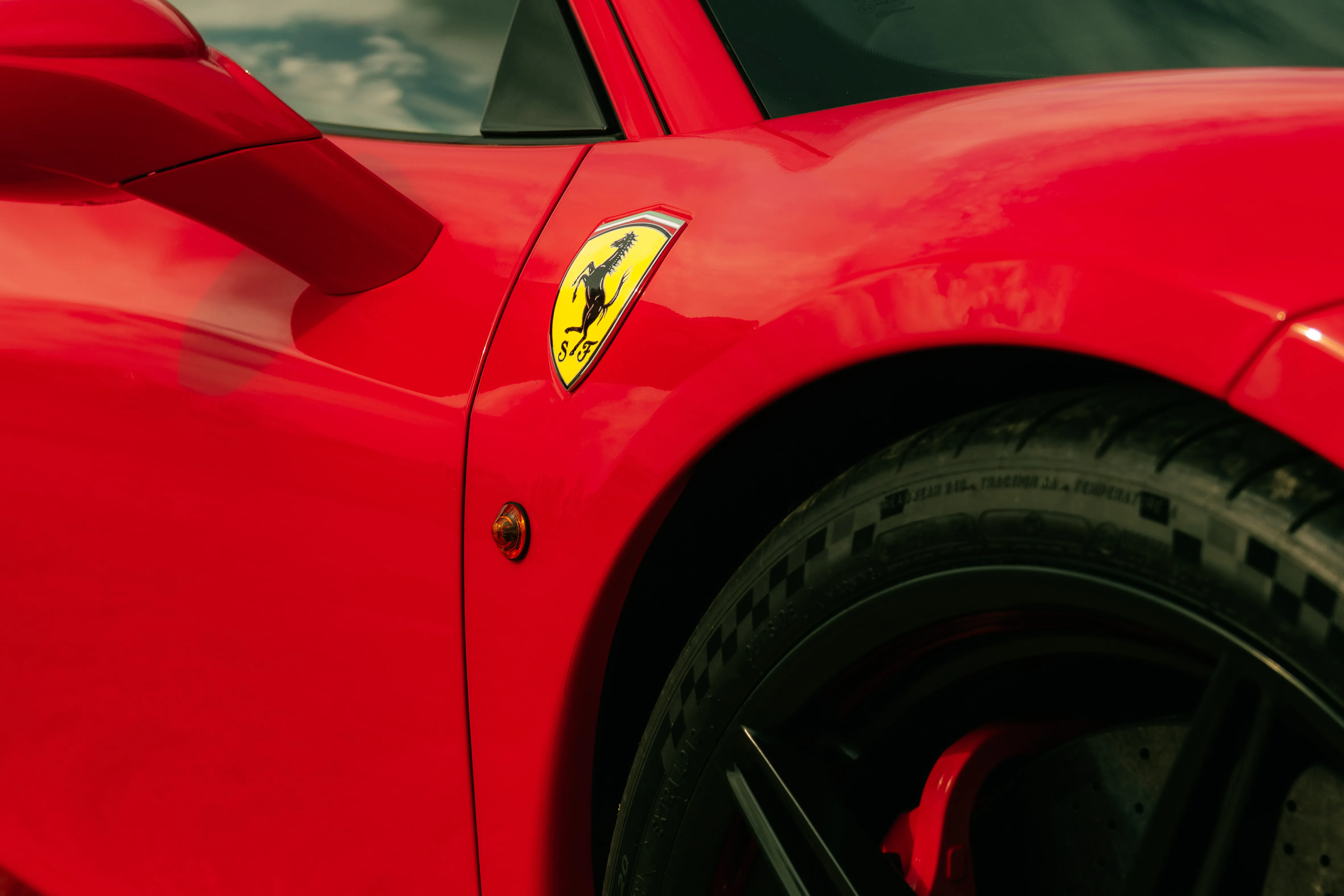 The Ferrari badge on the red wing of a sports car, wheel and brake calliper below.