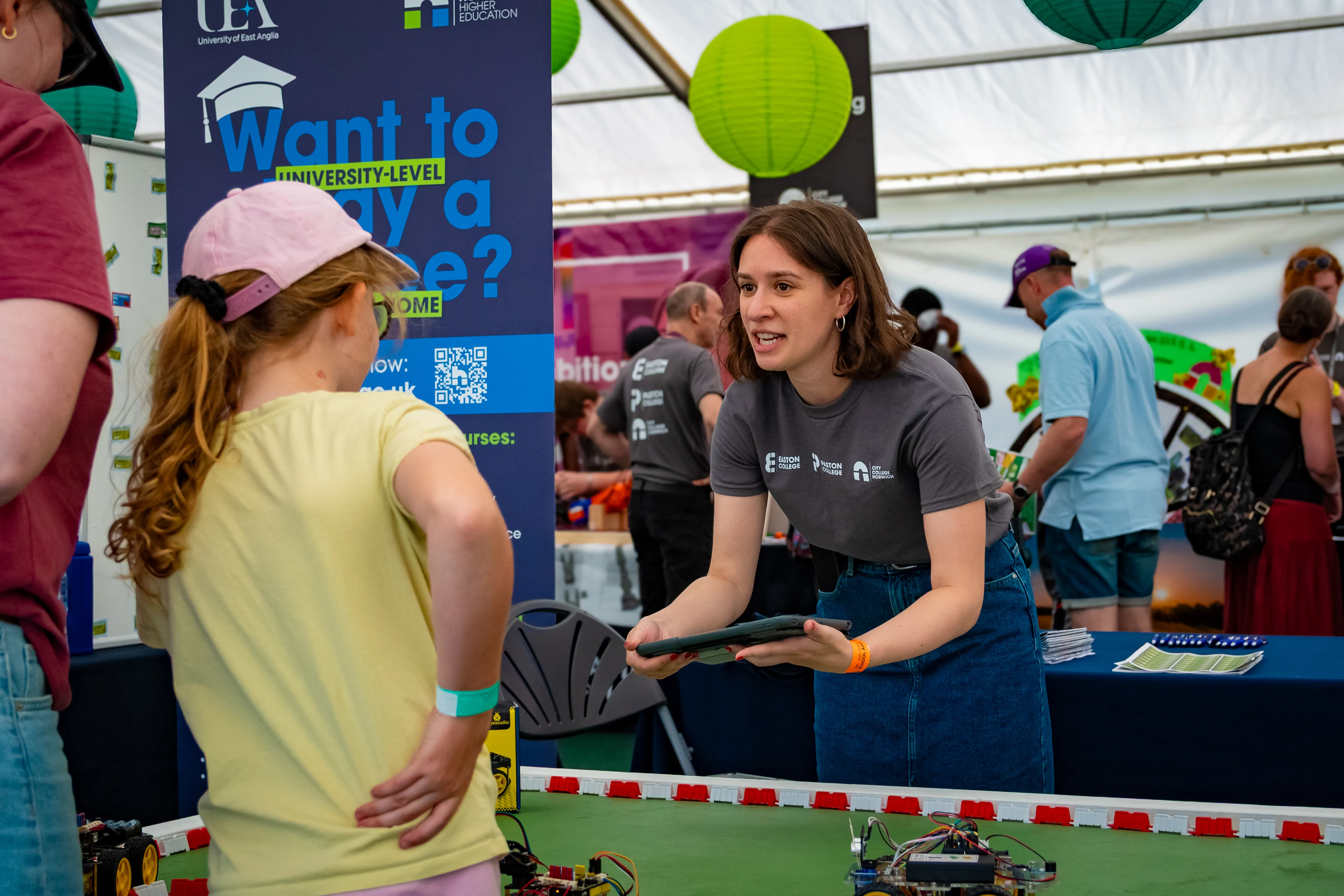 A young visitor chatting with staff at a university stand inside an exhibition tent.