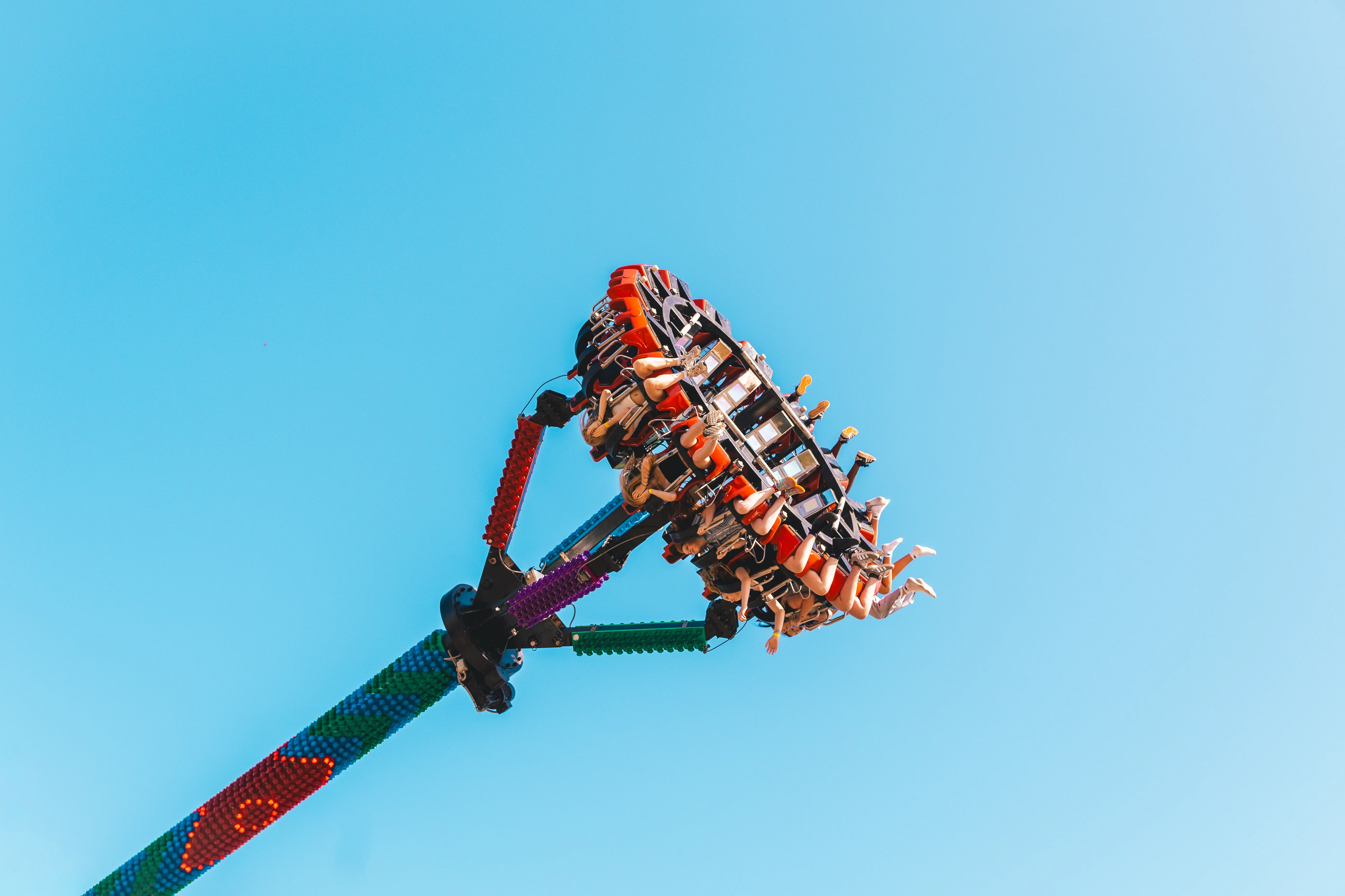 A fairground swing ride tilted high against a clear blue sky, riders strapped into its arm.