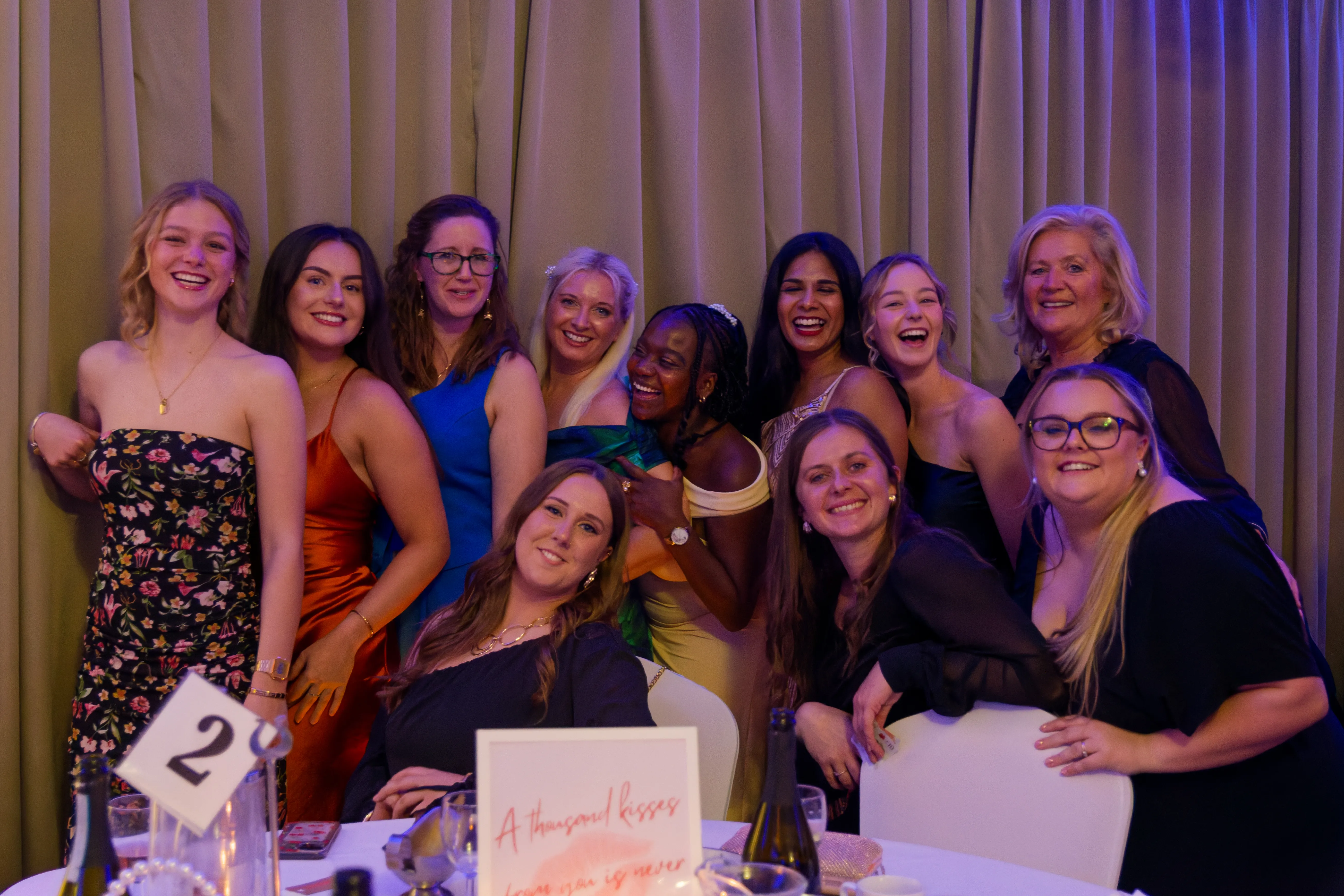 A group of friends in evening dresses posing together around their table.