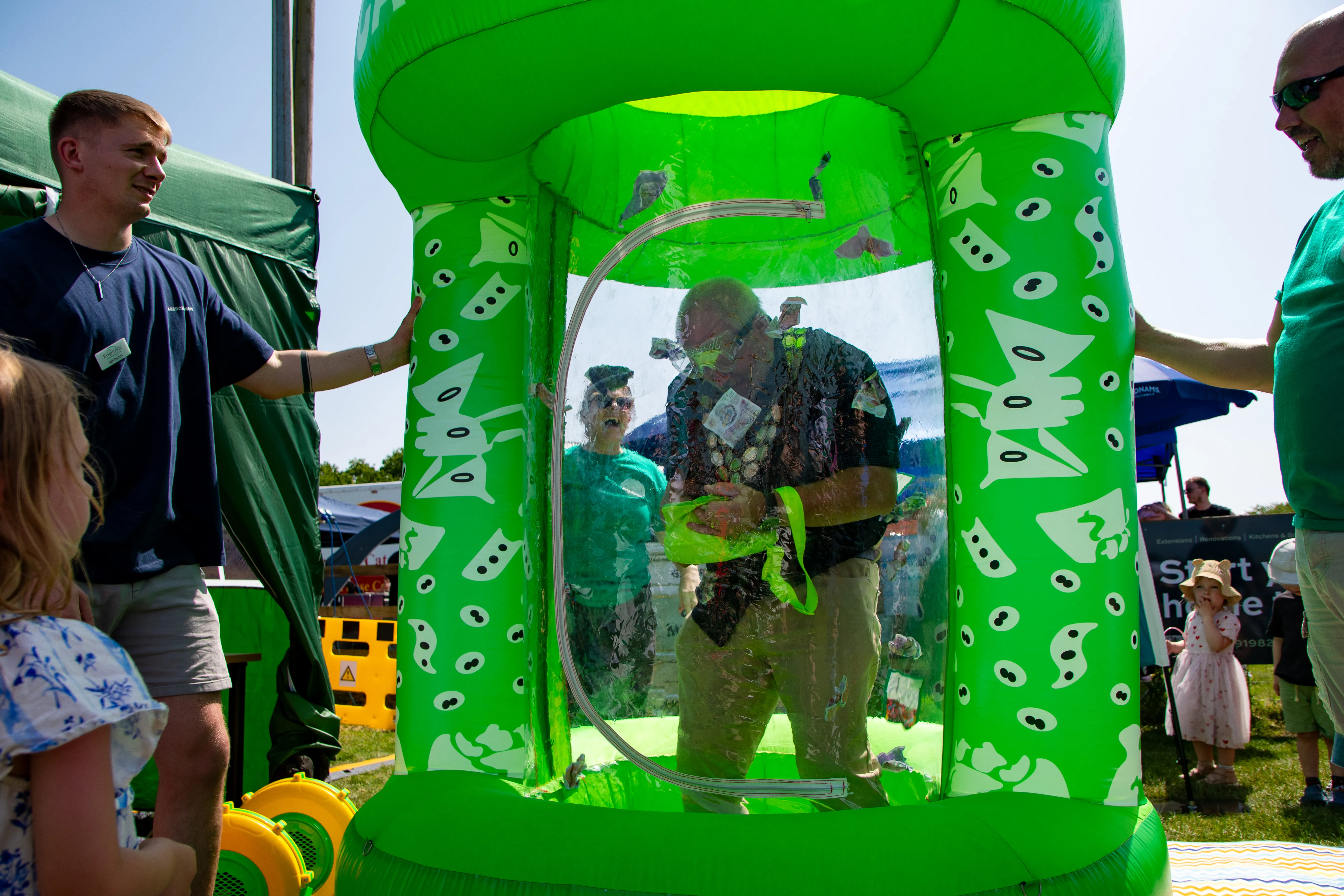 A man grabbing at flying notes inside a green inflatable cash-grab machine.