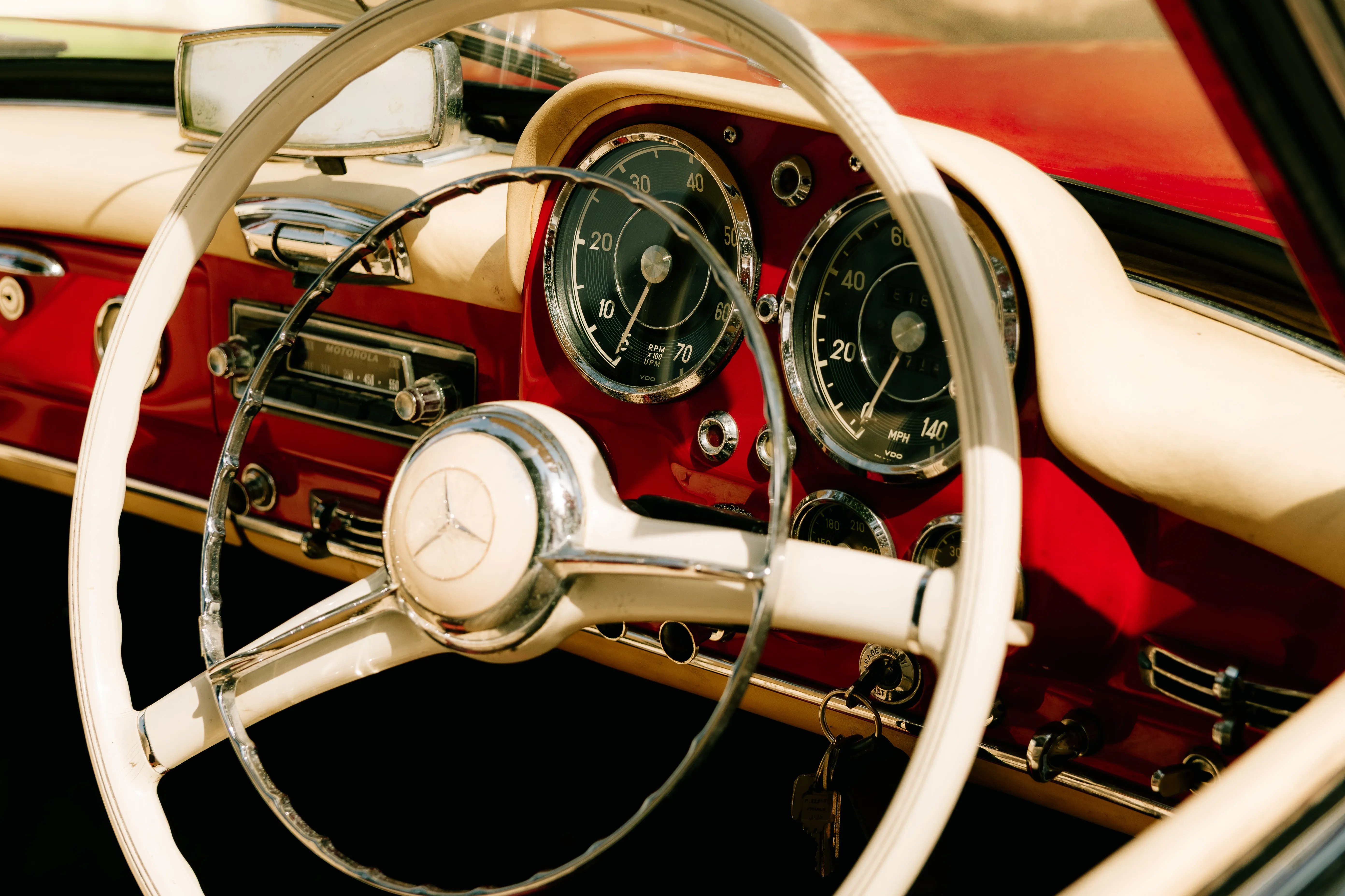 The white steering wheel and deep red dash of a classic Mercedes, chrome dials catching the sun.