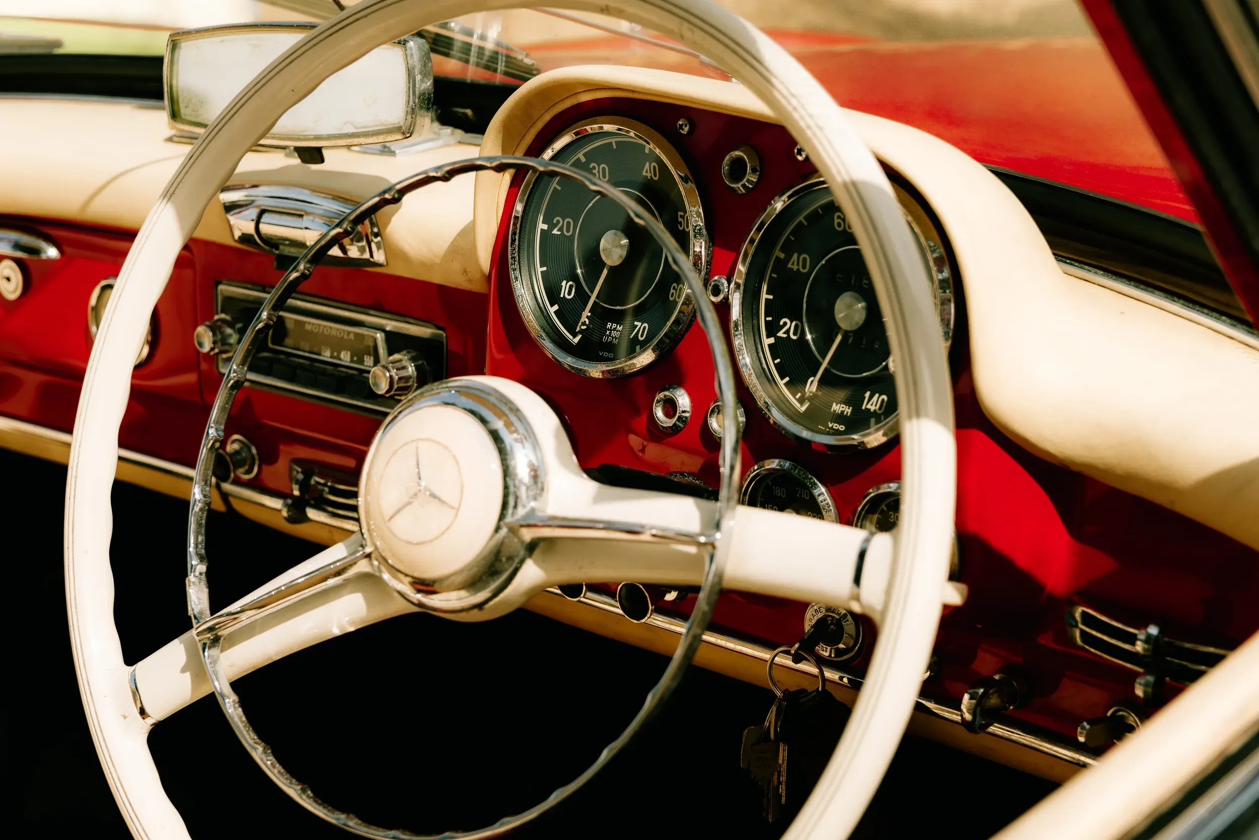 The white steering wheel and deep red dash of a classic Mercedes, chrome dials catching the sun.