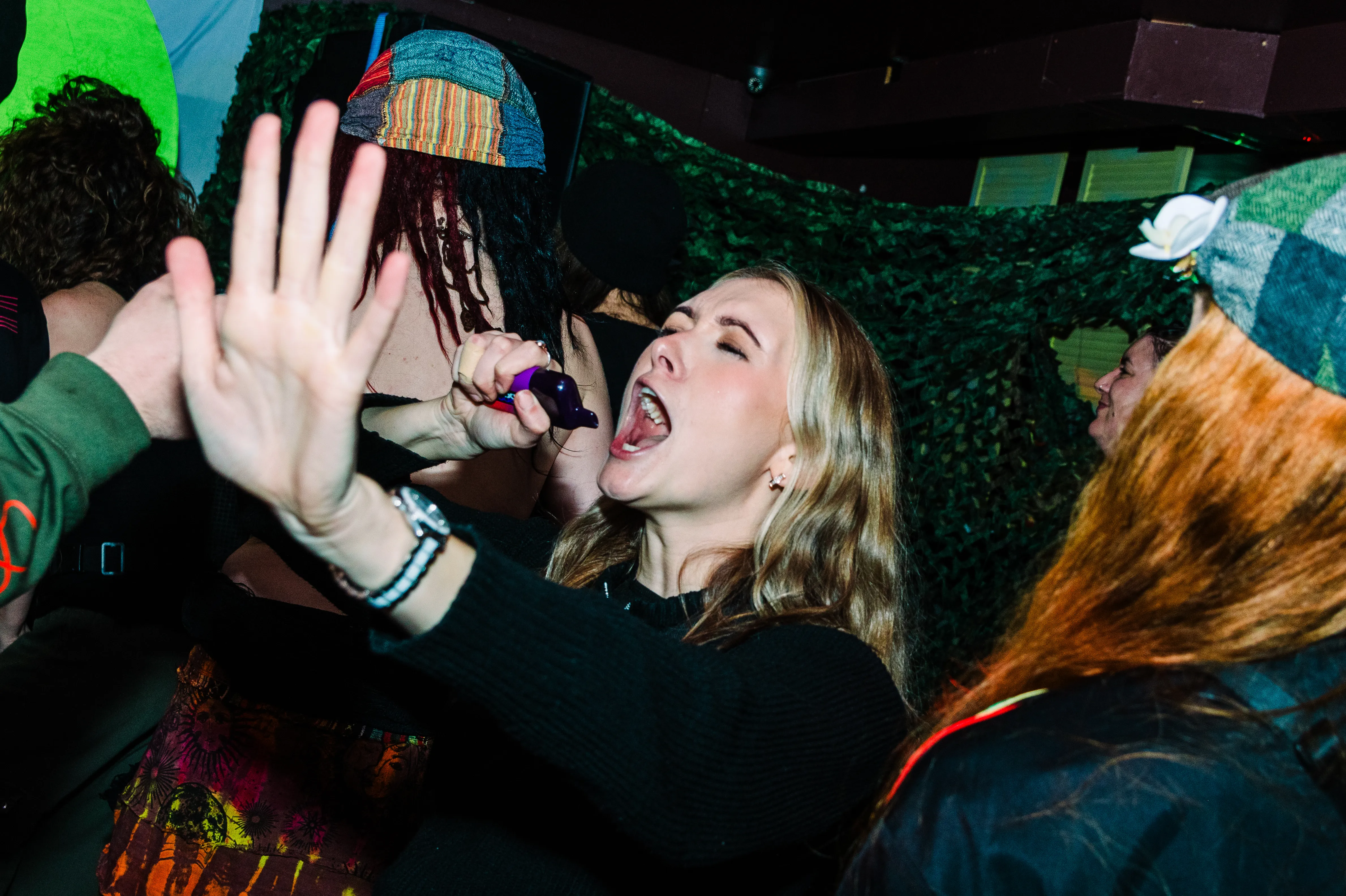 A woman singing along mid-laugh, a friend's hand raised in front of the lens.