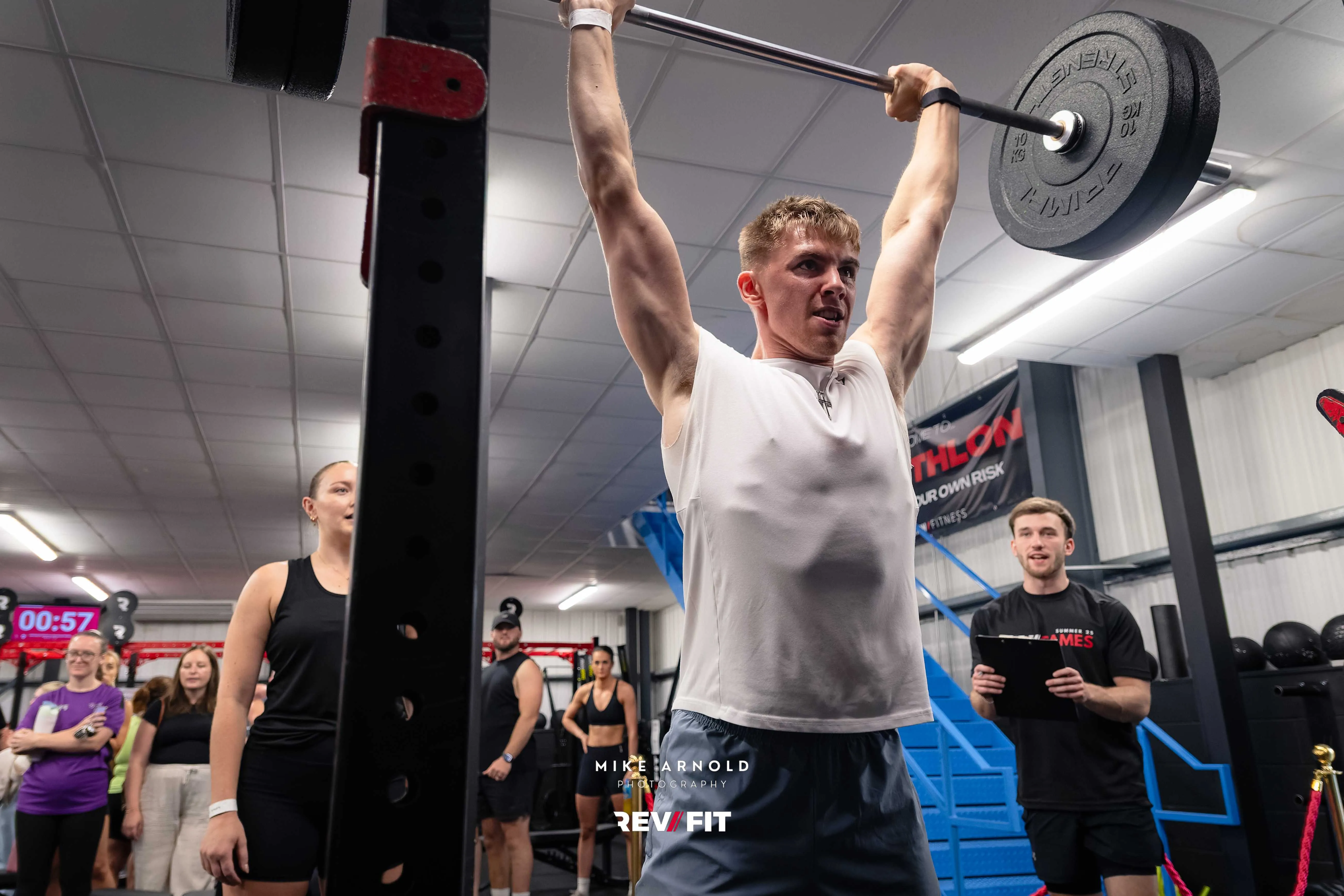 A competitor locking a barbell out overhead beside the competition clock.