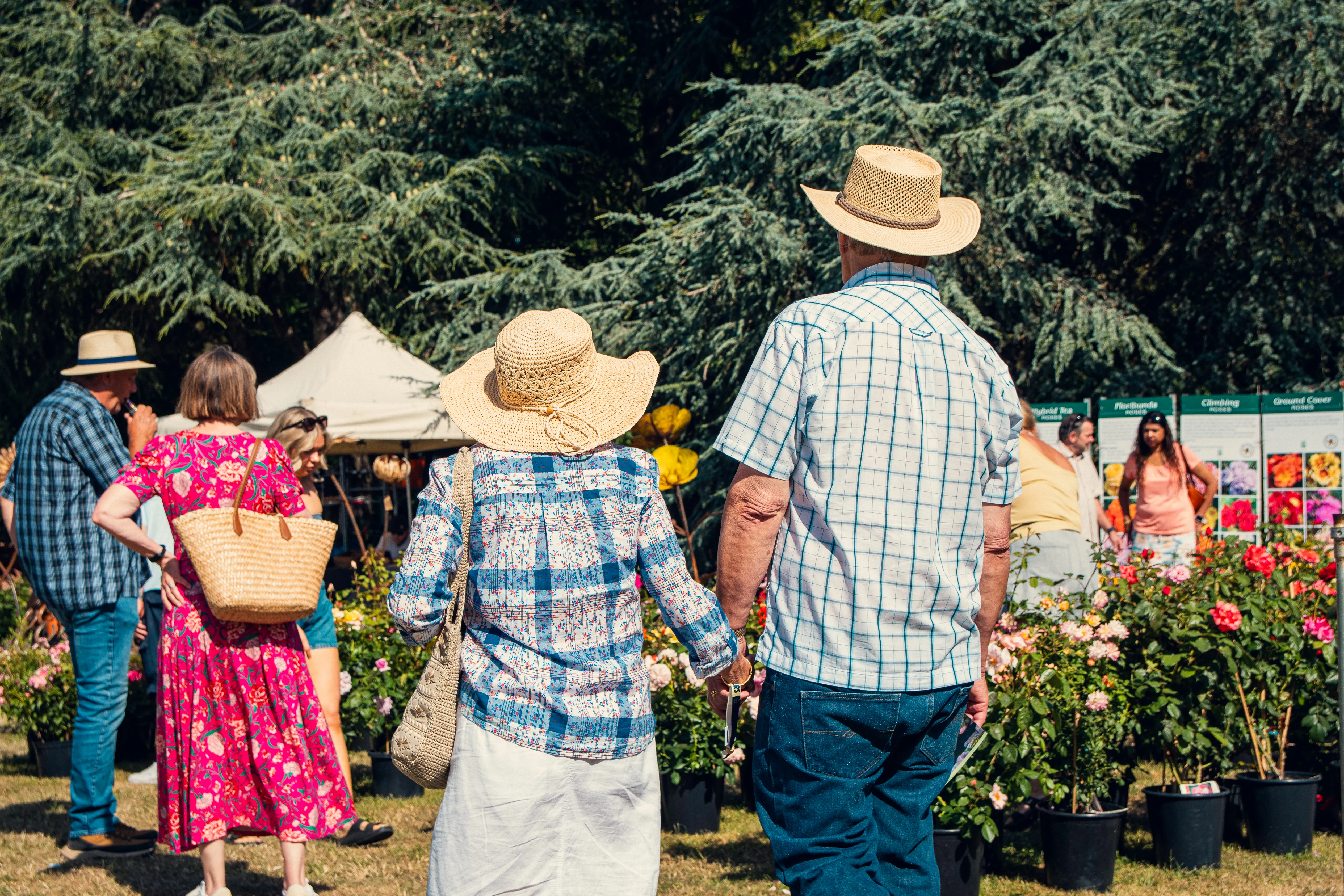 Visitors in sun hats browsing rose displays in the flower garden area.