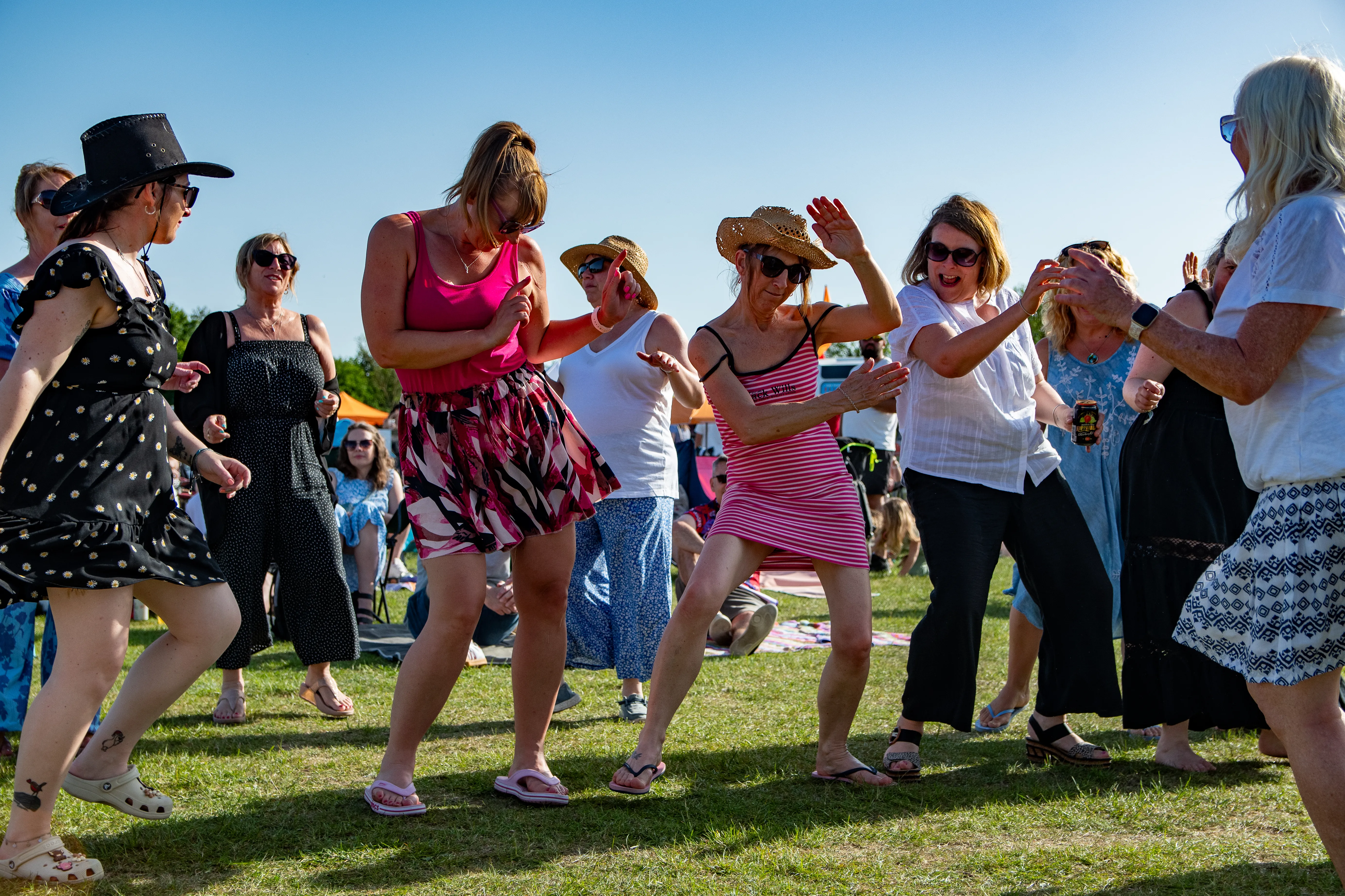 A group of women dancing together outdoors in the sun at a summer festival.