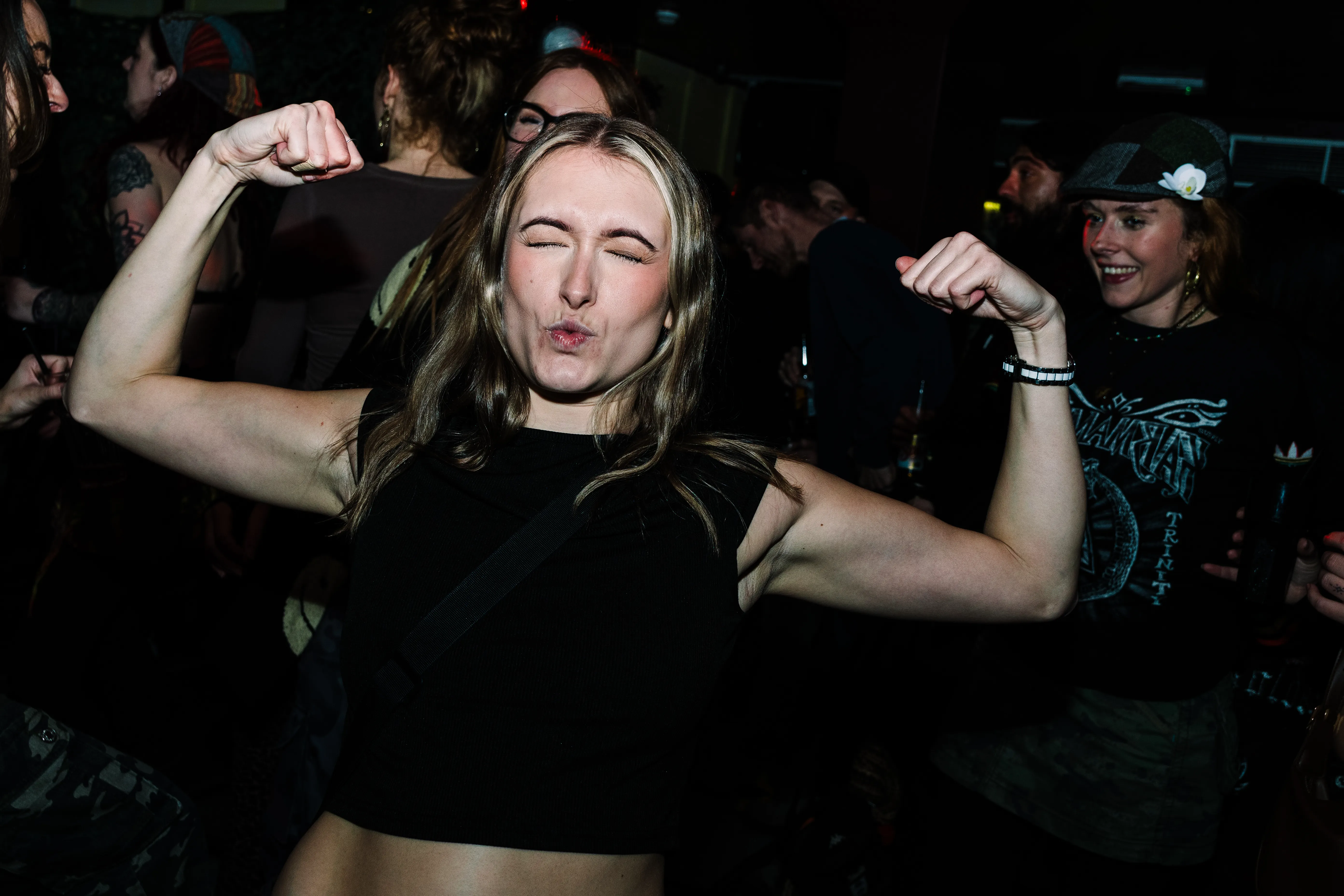 A woman winking and flexing both arms on the dancefloor.
