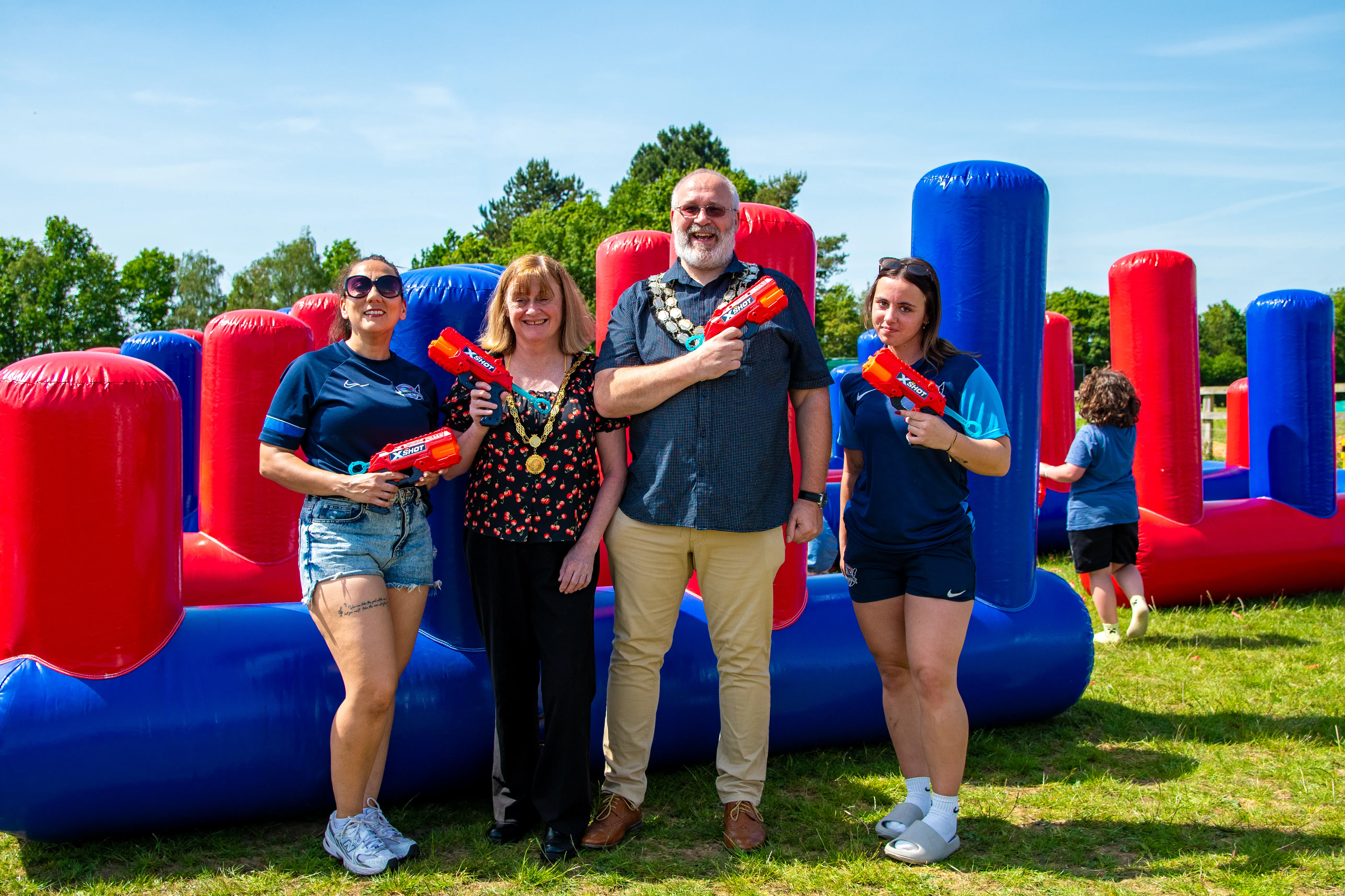 A family posing with red water pistols in front of an inflatable battle run.