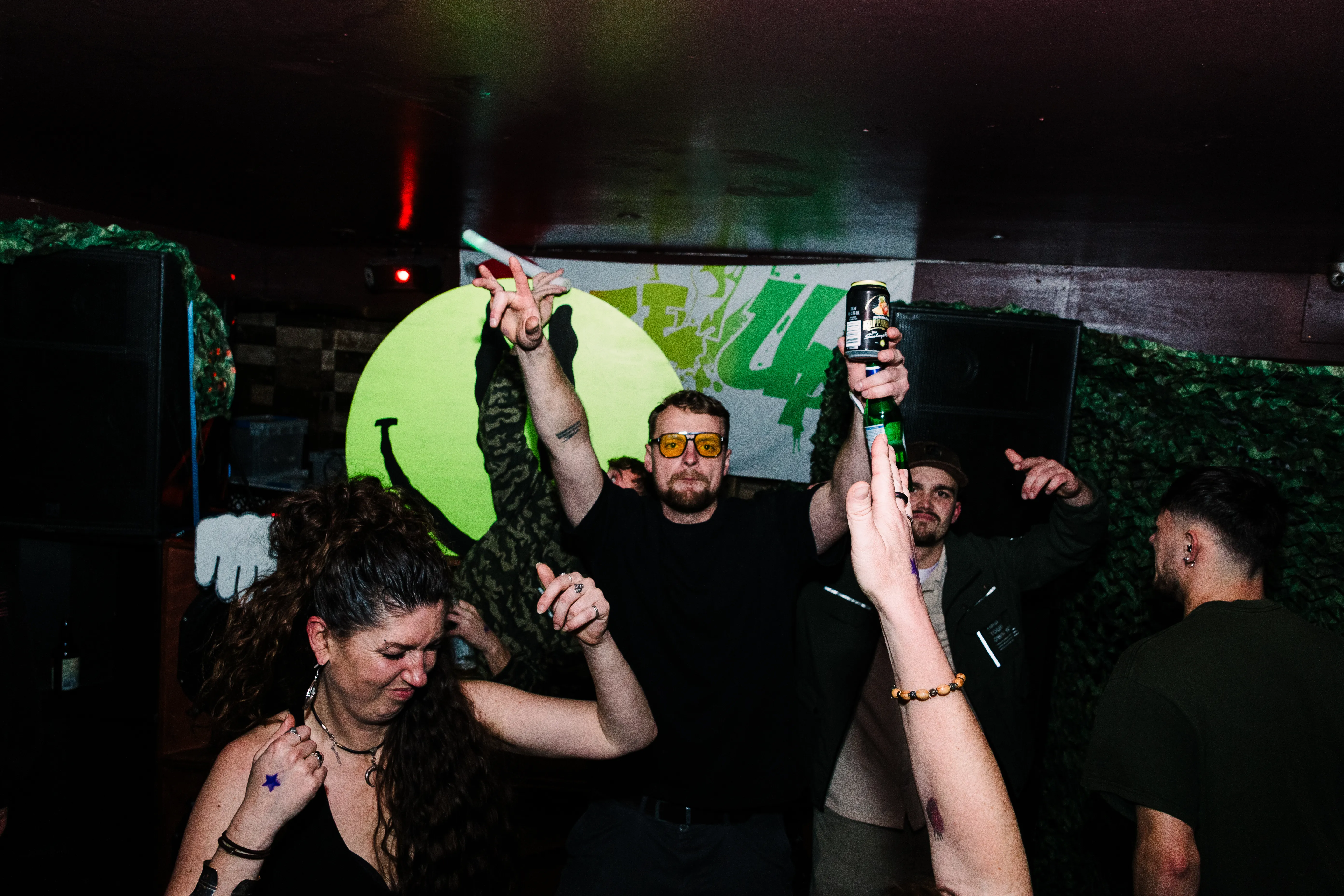 Dancers mid-move under the venue's green logo, arms up in the low light.