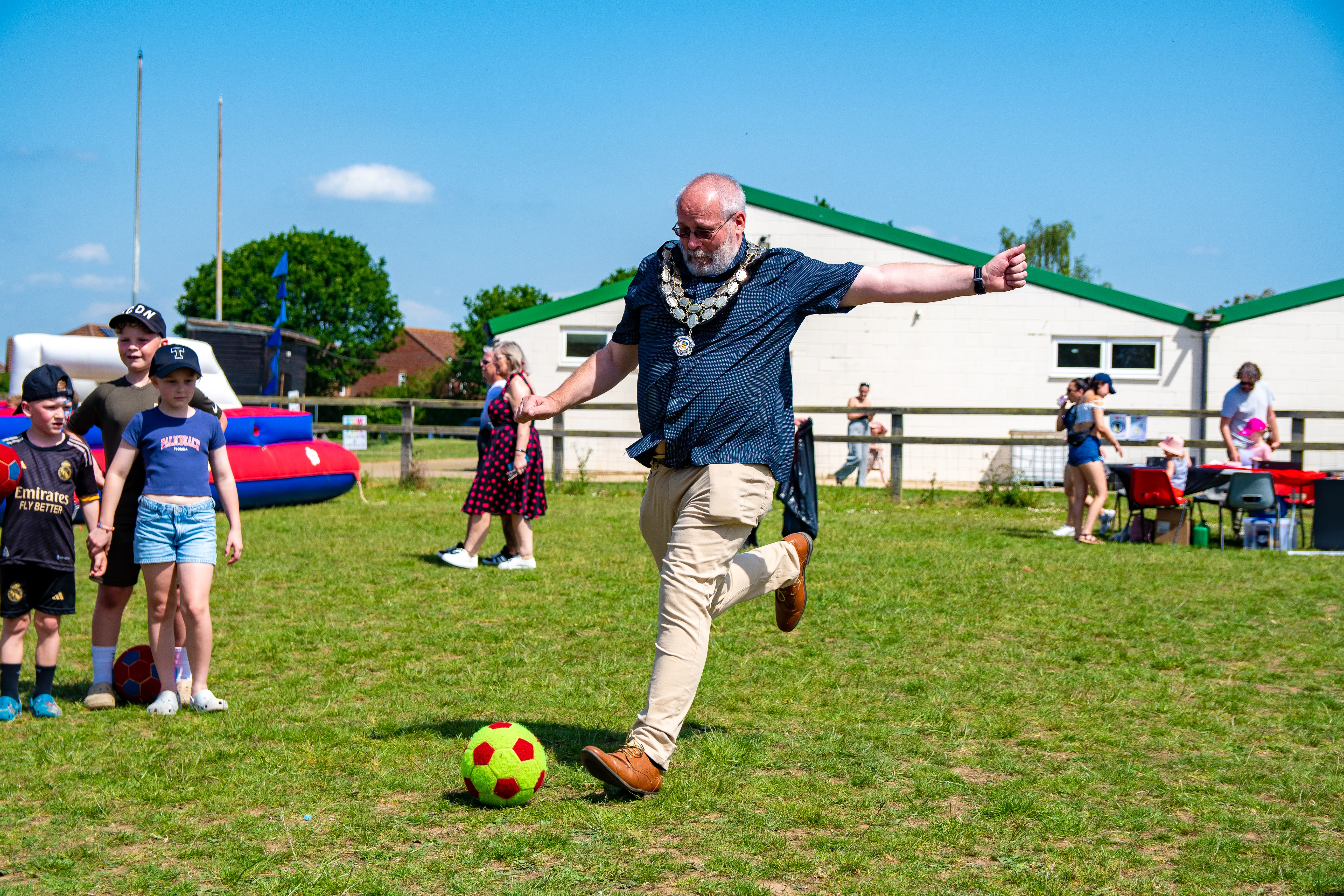 The mayor mid-kick with a football on the festival field.