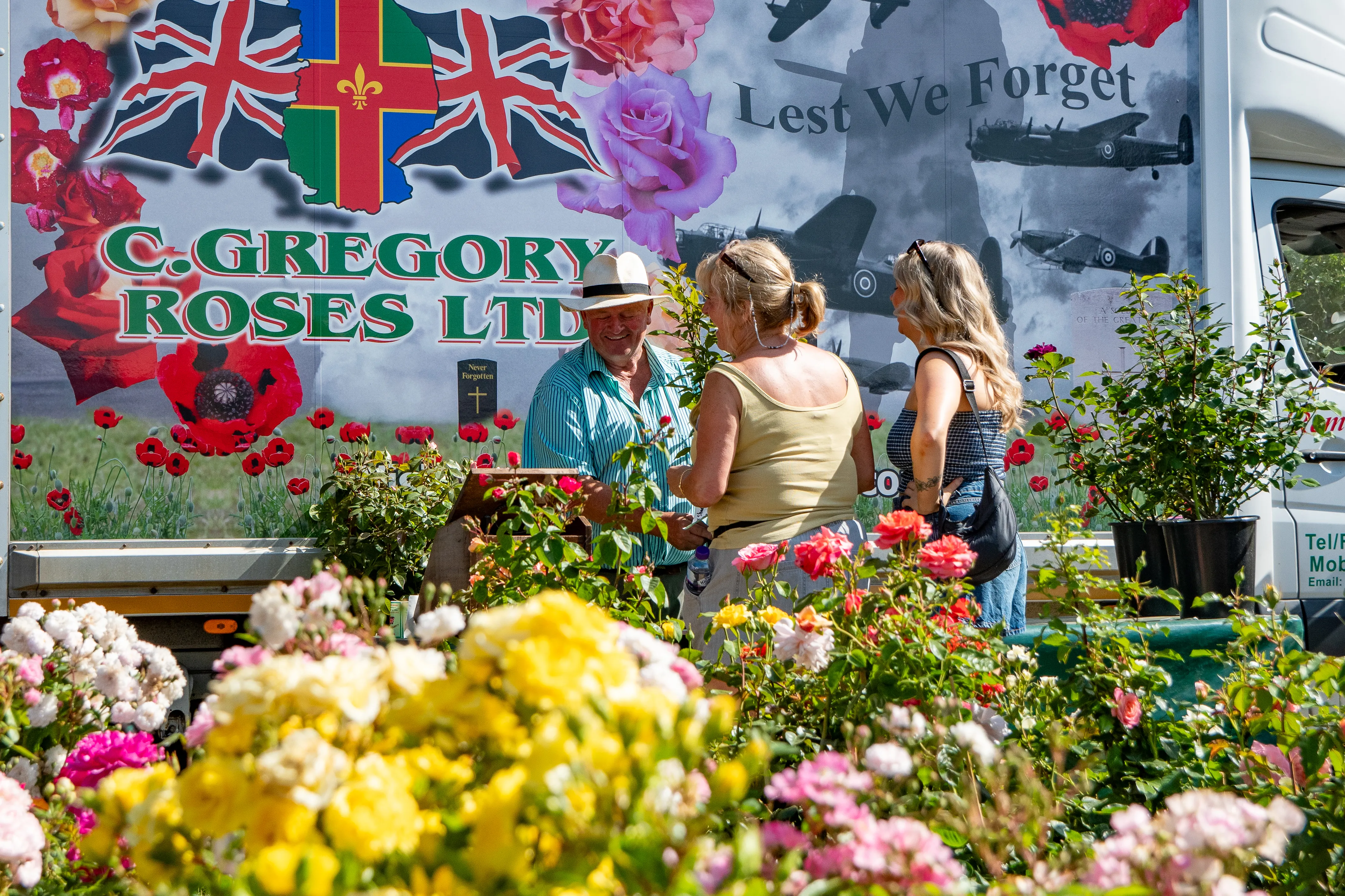 Customers chatting at a rose grower's stall, flowers banked up in the foreground.