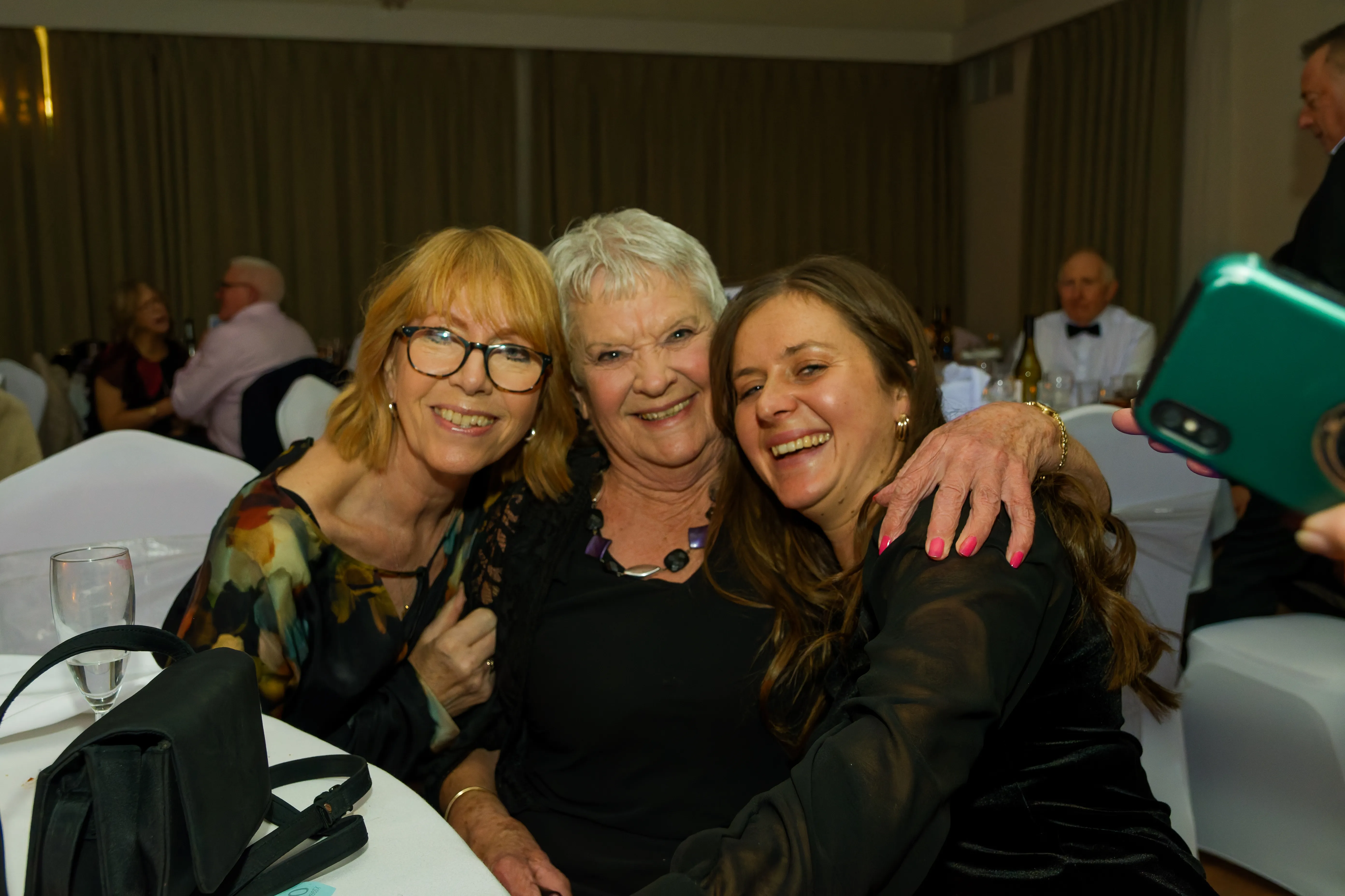 Three friends hugging close at their table, laughing.