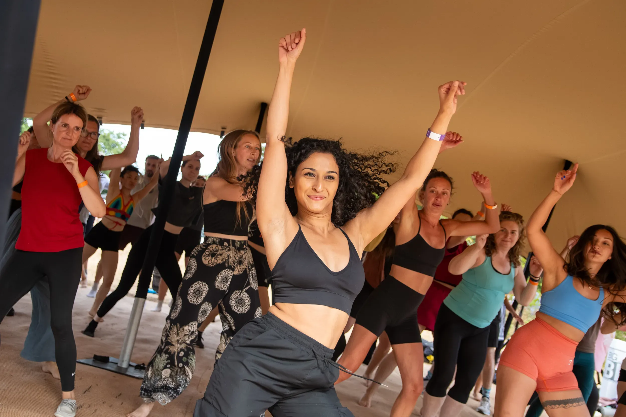 A woman dancing with both arms in the air in the middle of a packed movement class.