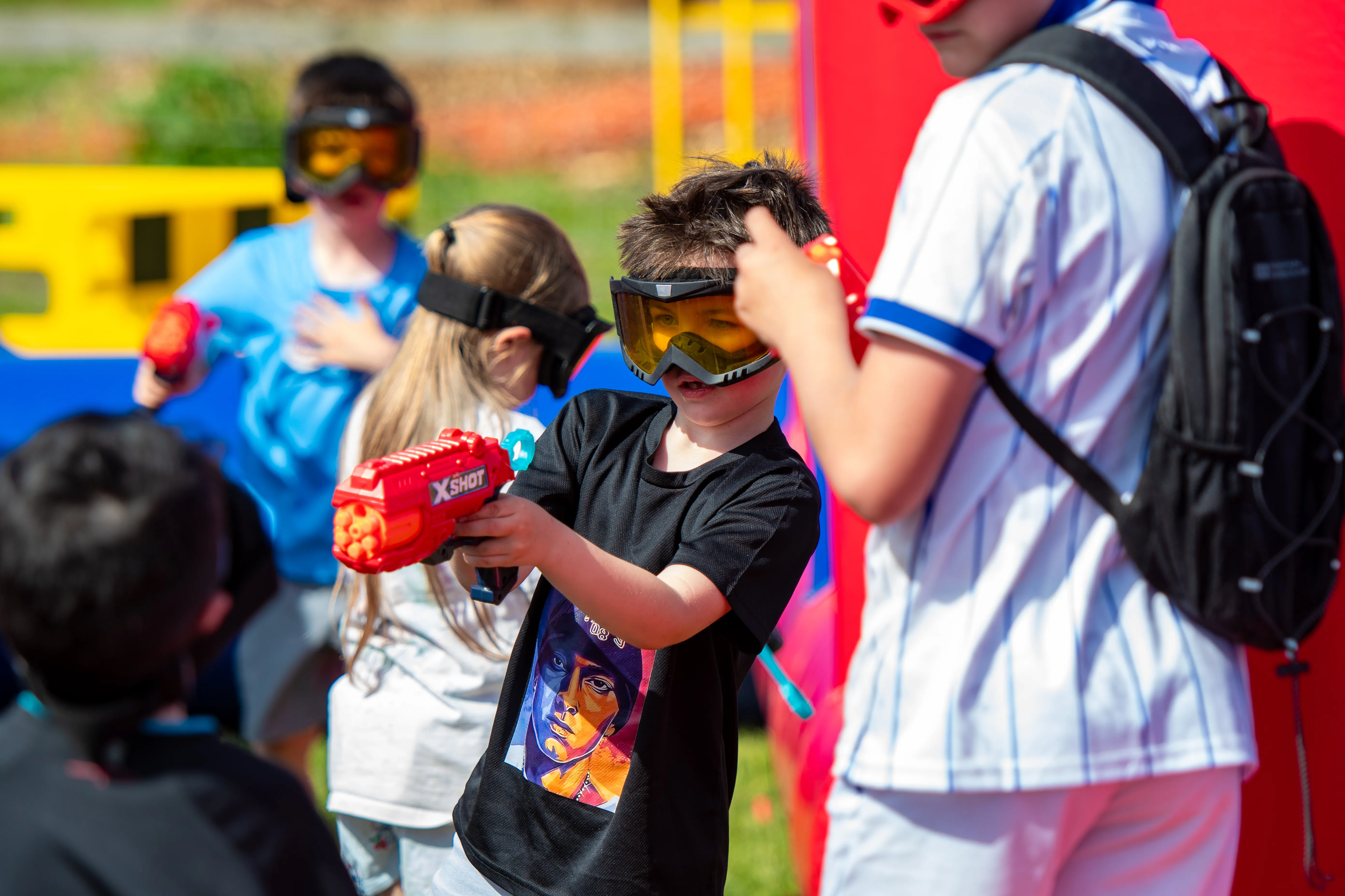 Children in safety glasses mid-battle with foam dart blasters.
