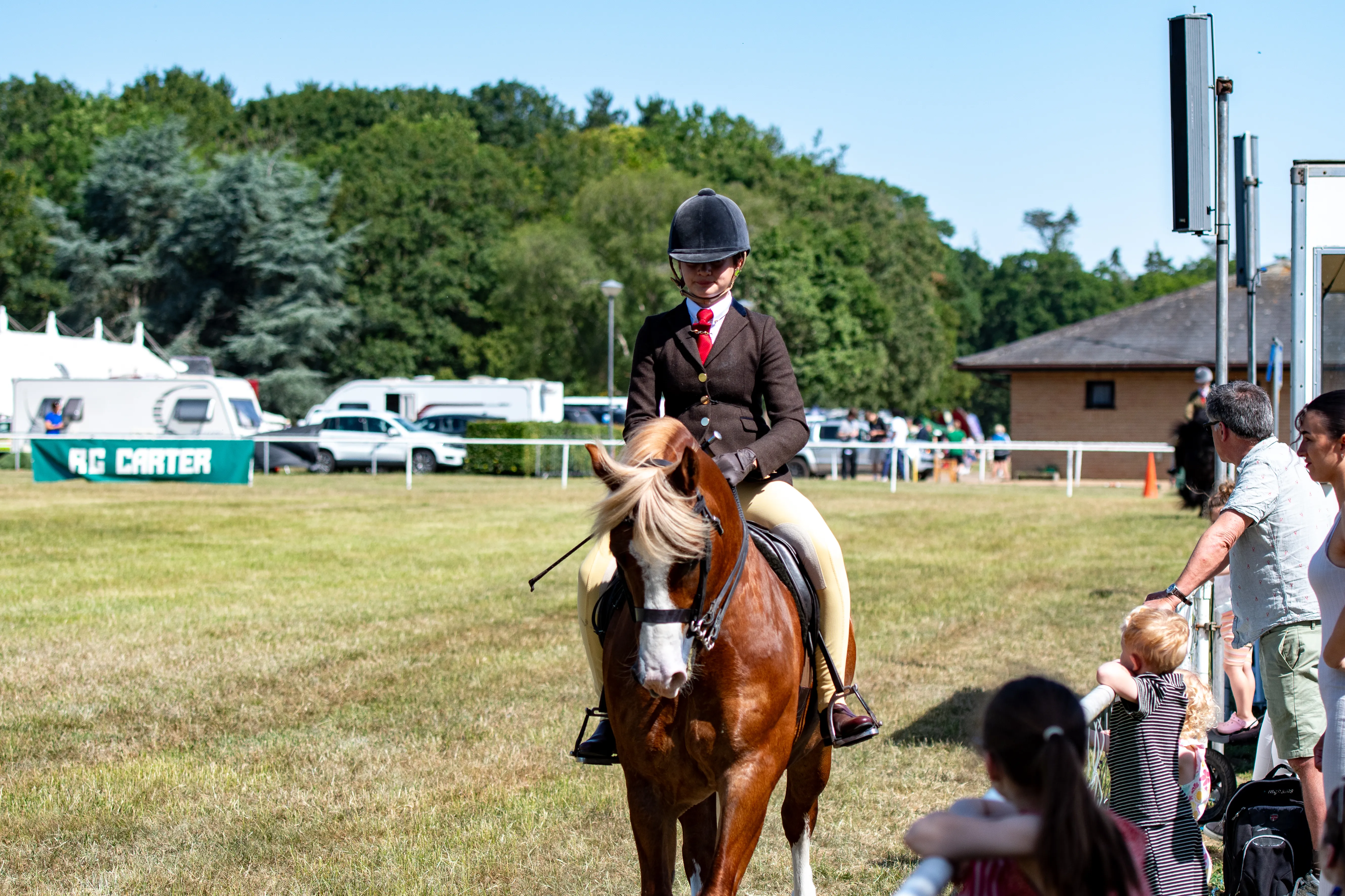 A young rider in show dress walking their pony past spectators.