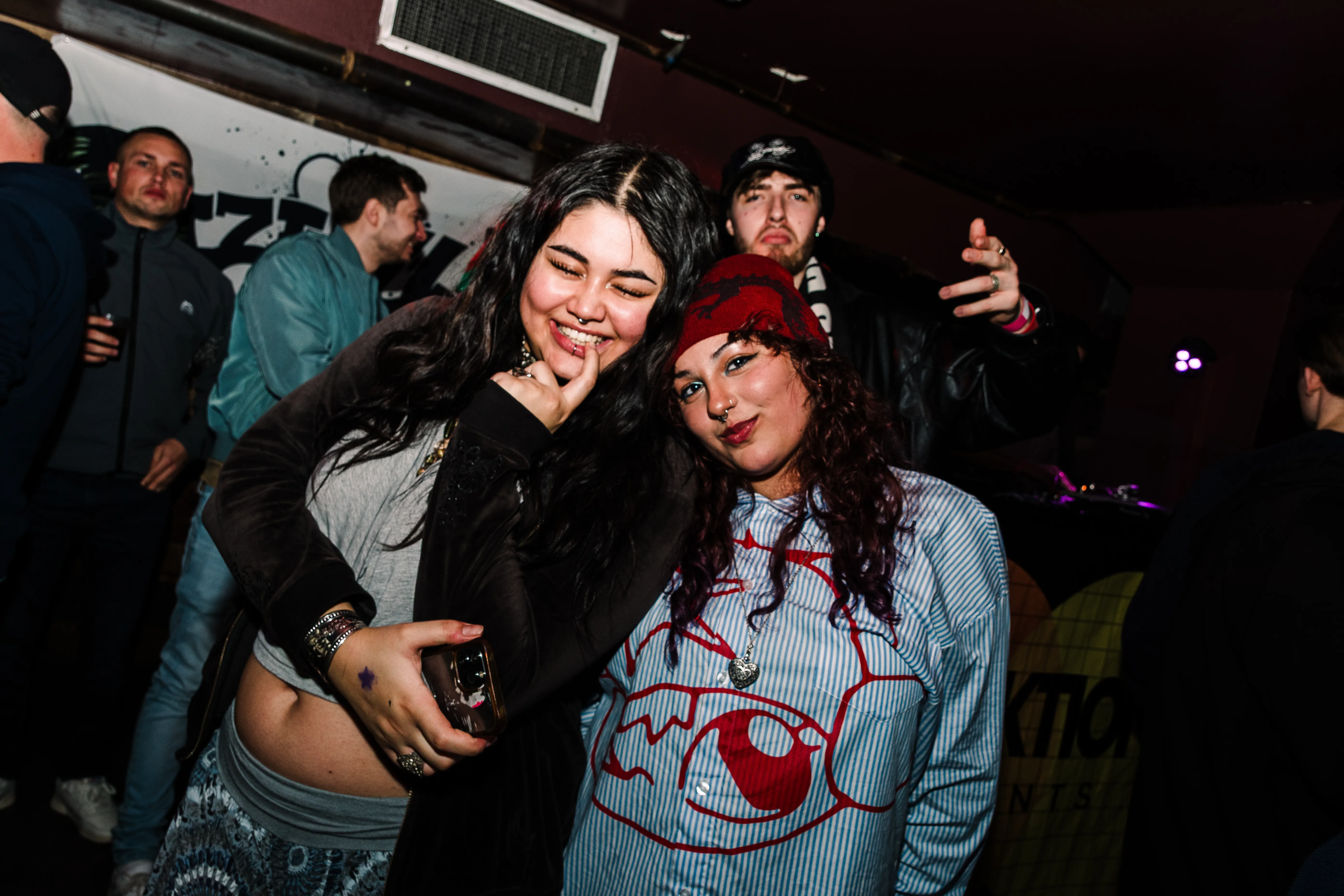 Two friends in winter hats pulling faces close to the camera on the dancefloor.