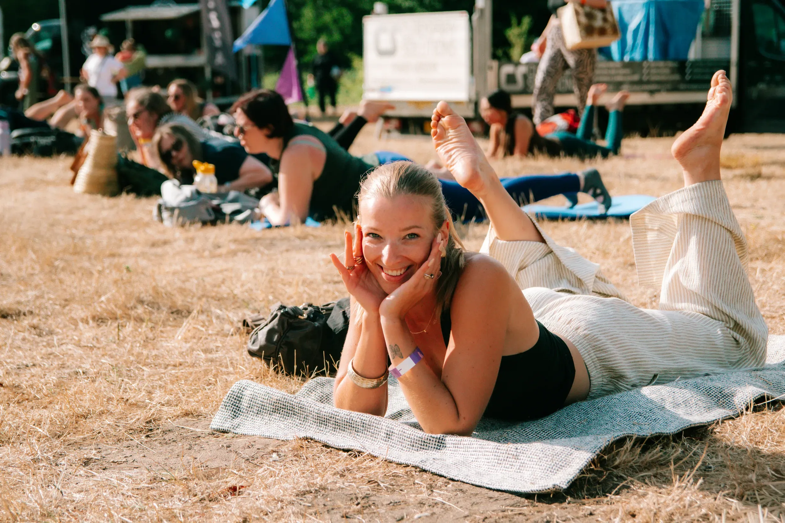 A festivalgoer stretched out on a blanket in the dry grass, chin resting on her hands, grinning at the camera.