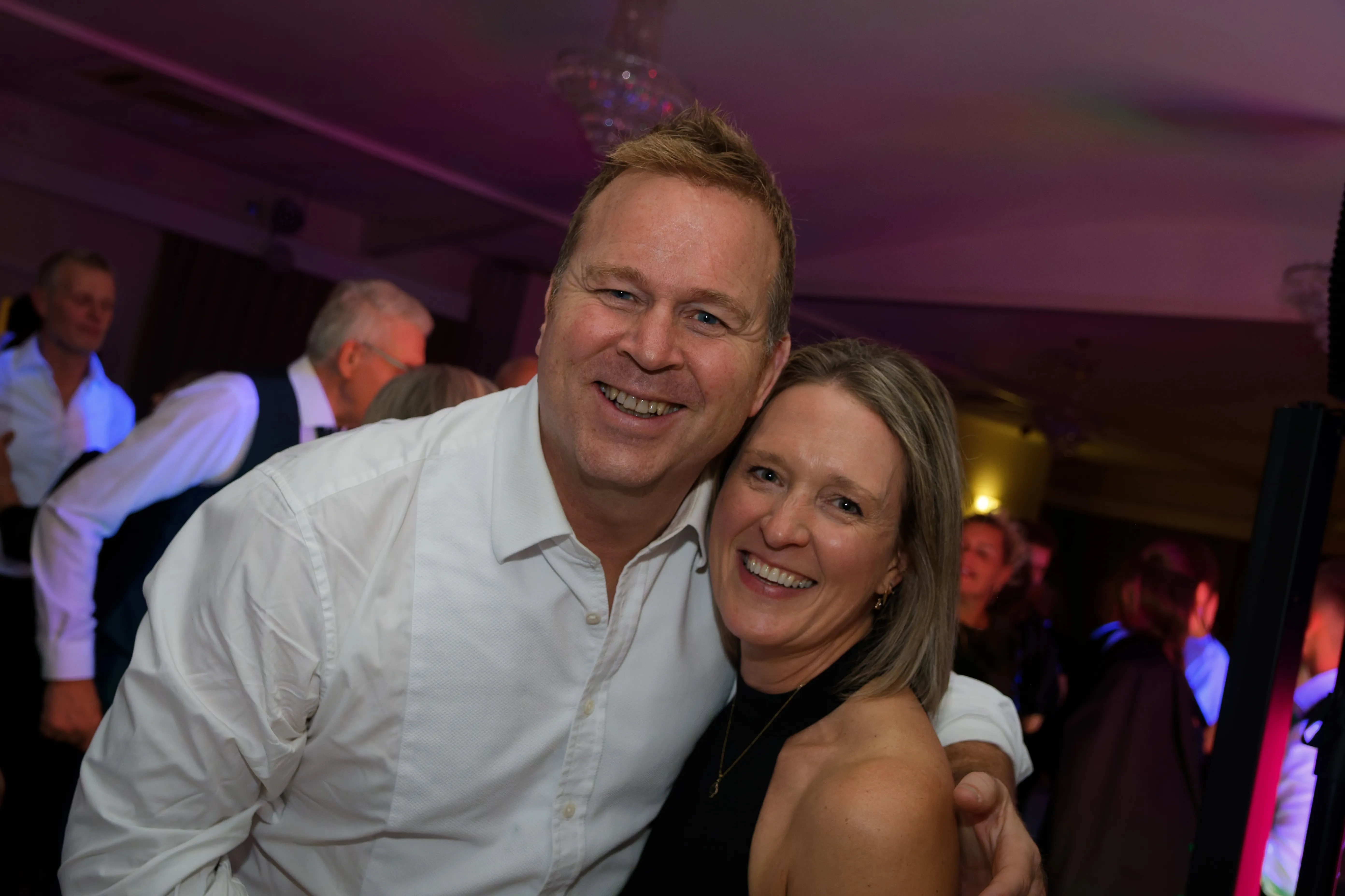 A couple hugging tightly on the dancefloor, both beaming.