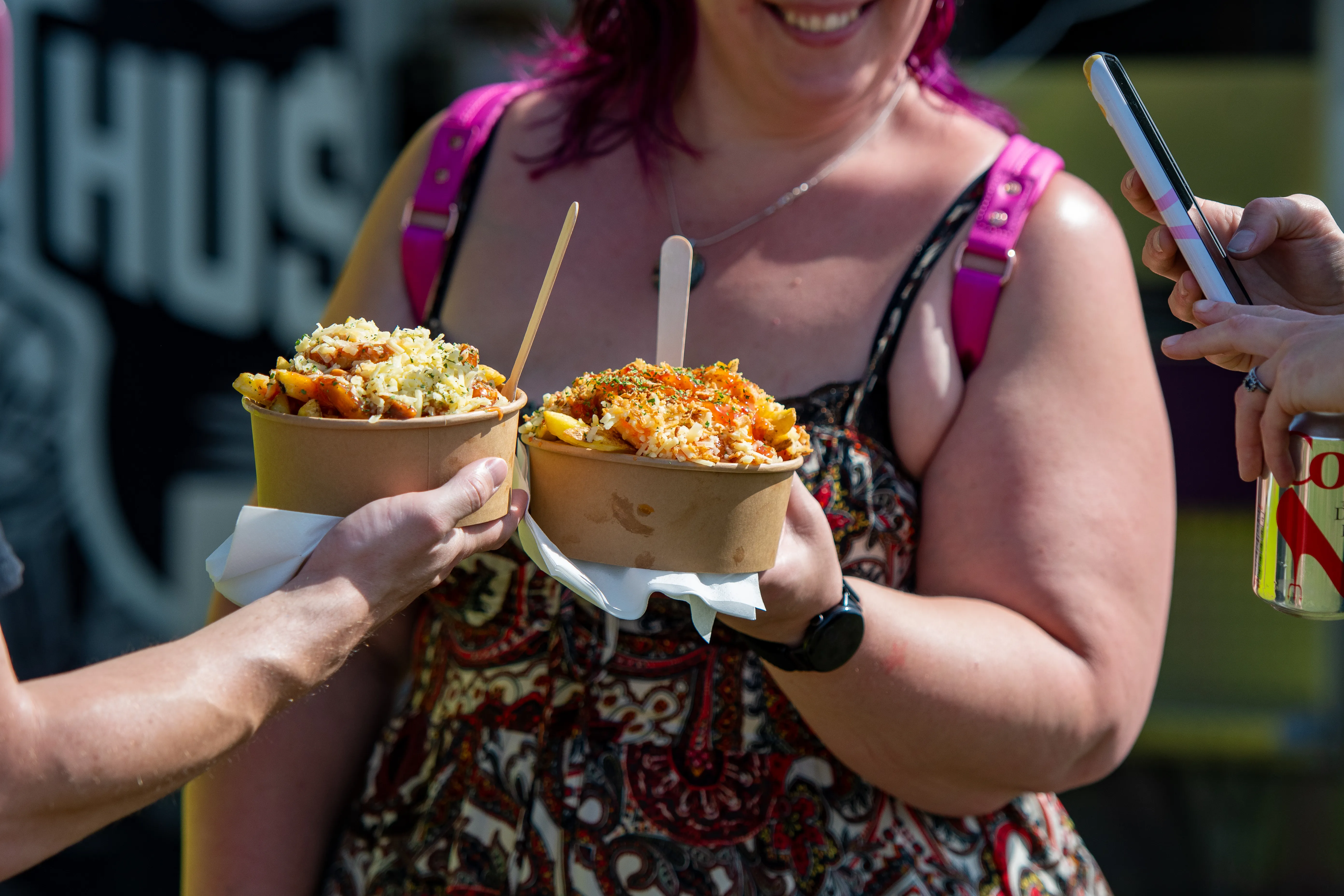 A festivalgoer carrying two tubs of loaded fries from the food stalls.