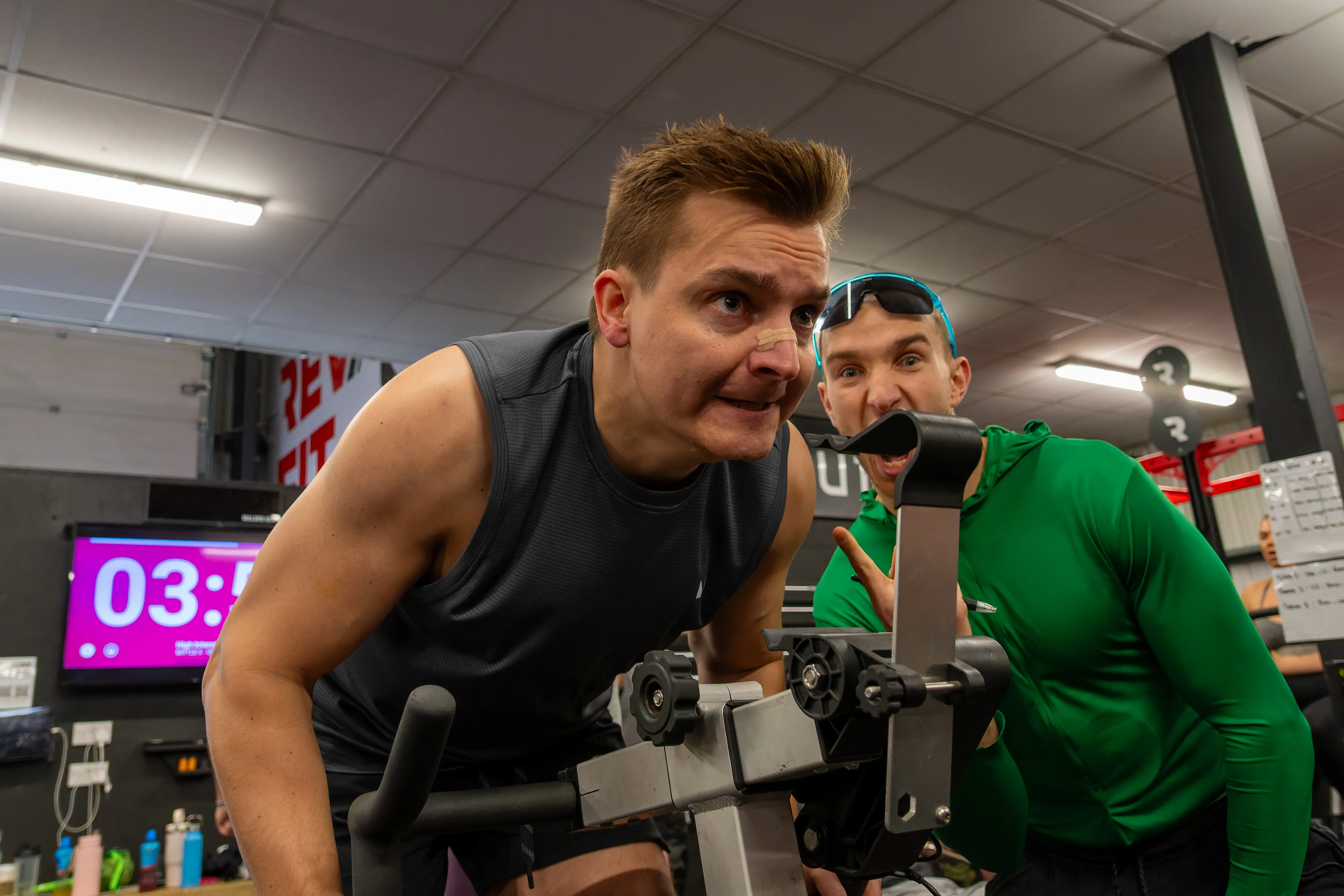 A competitor grimacing through a sprint on the assault bike, the clock behind him.