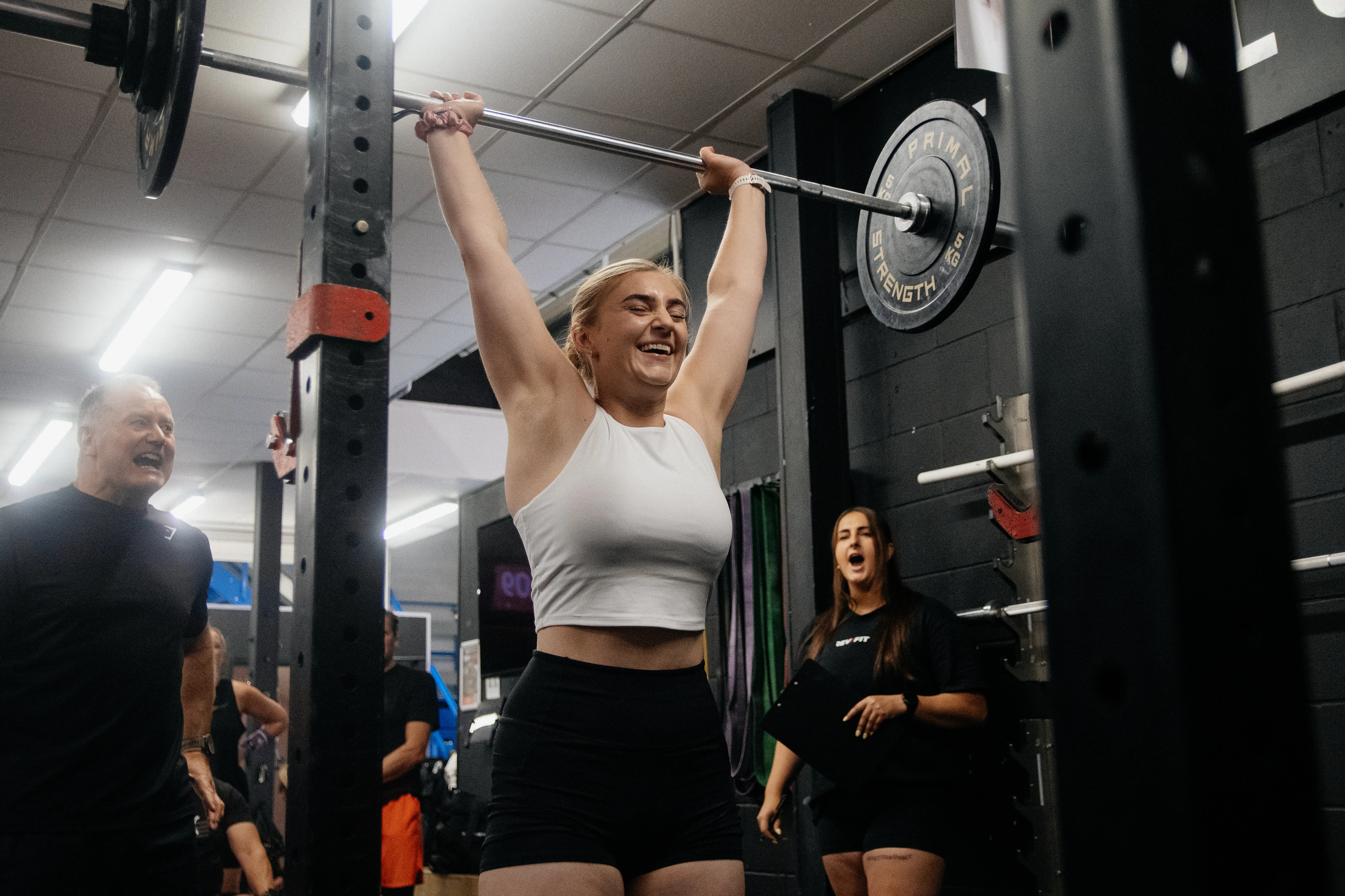 A gym competitor locking a barbell out overhead during a fitness competition.