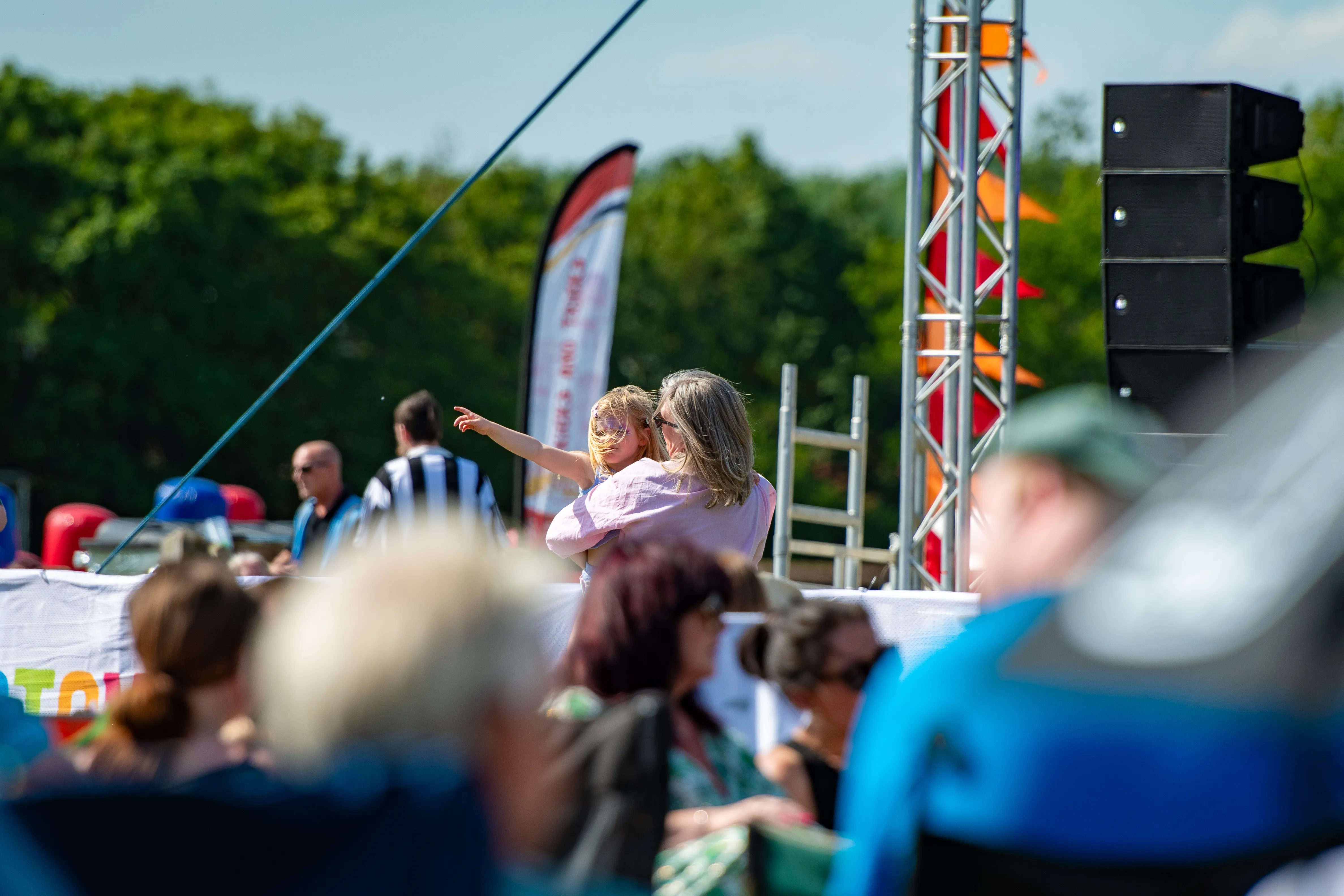 Festivalgoers gathered near the stage rigging under a blue sky.
