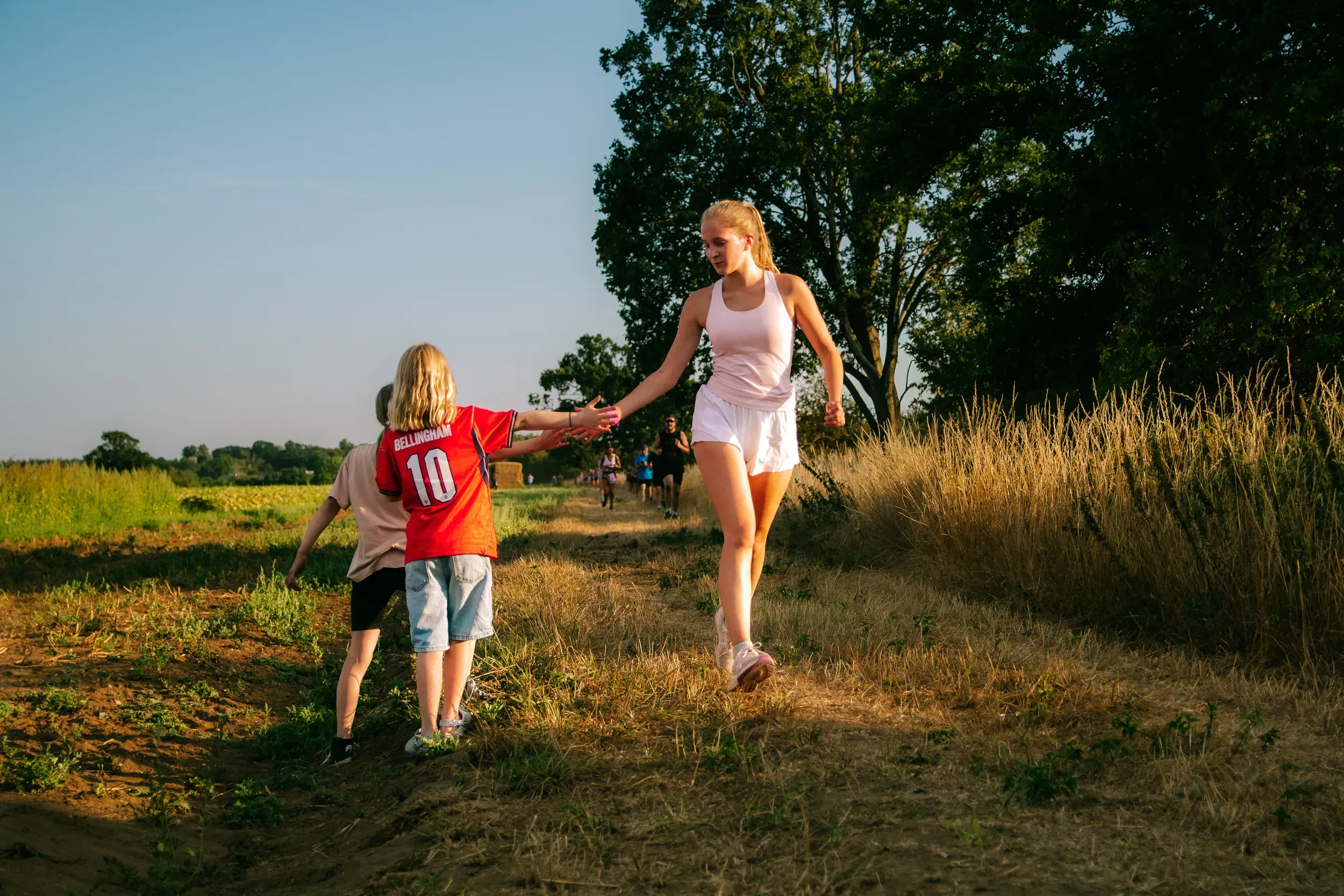 A young girl reaching up to high-five a runner coming past on the track.