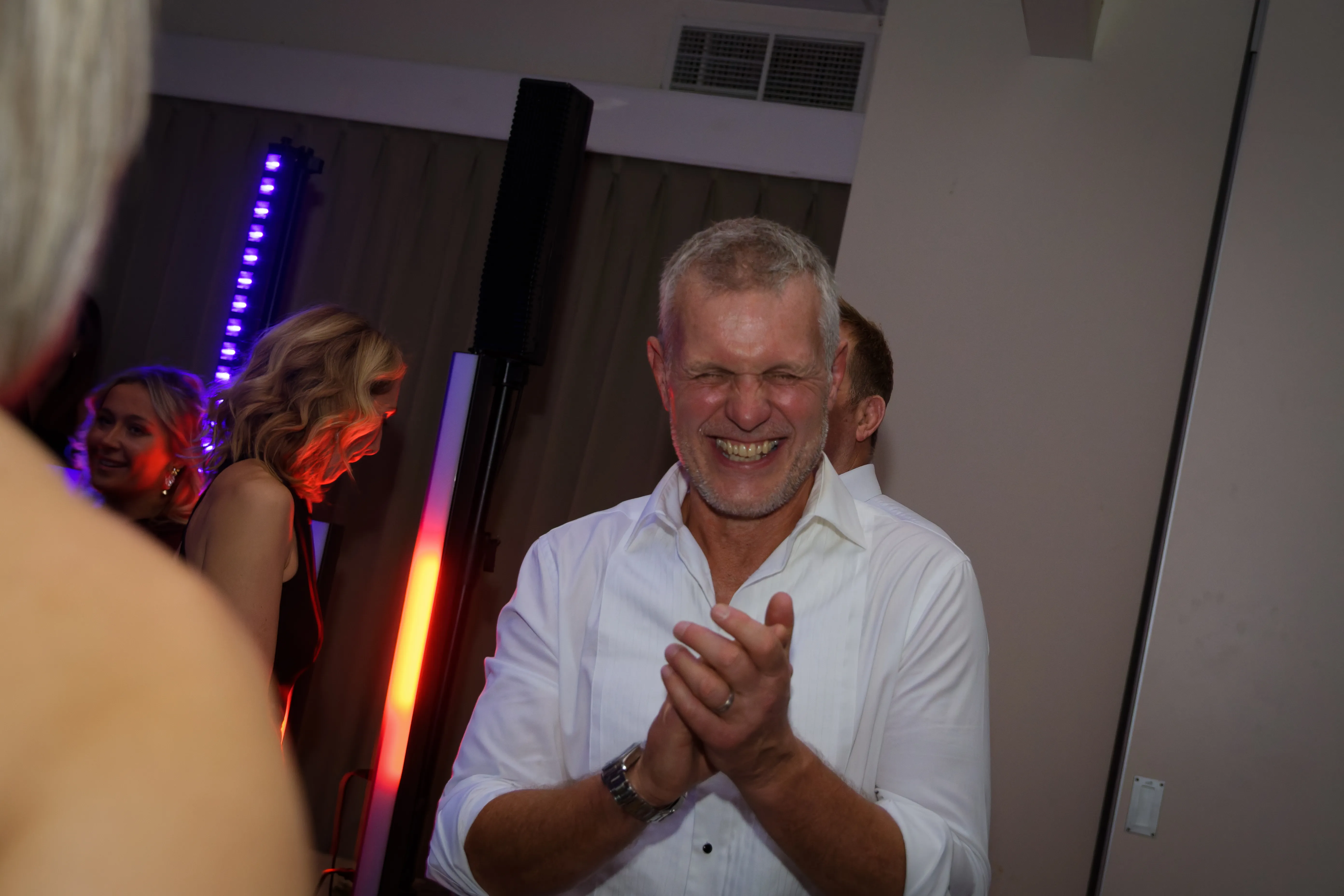 A man in a white shirt clapping and laughing mid-song.