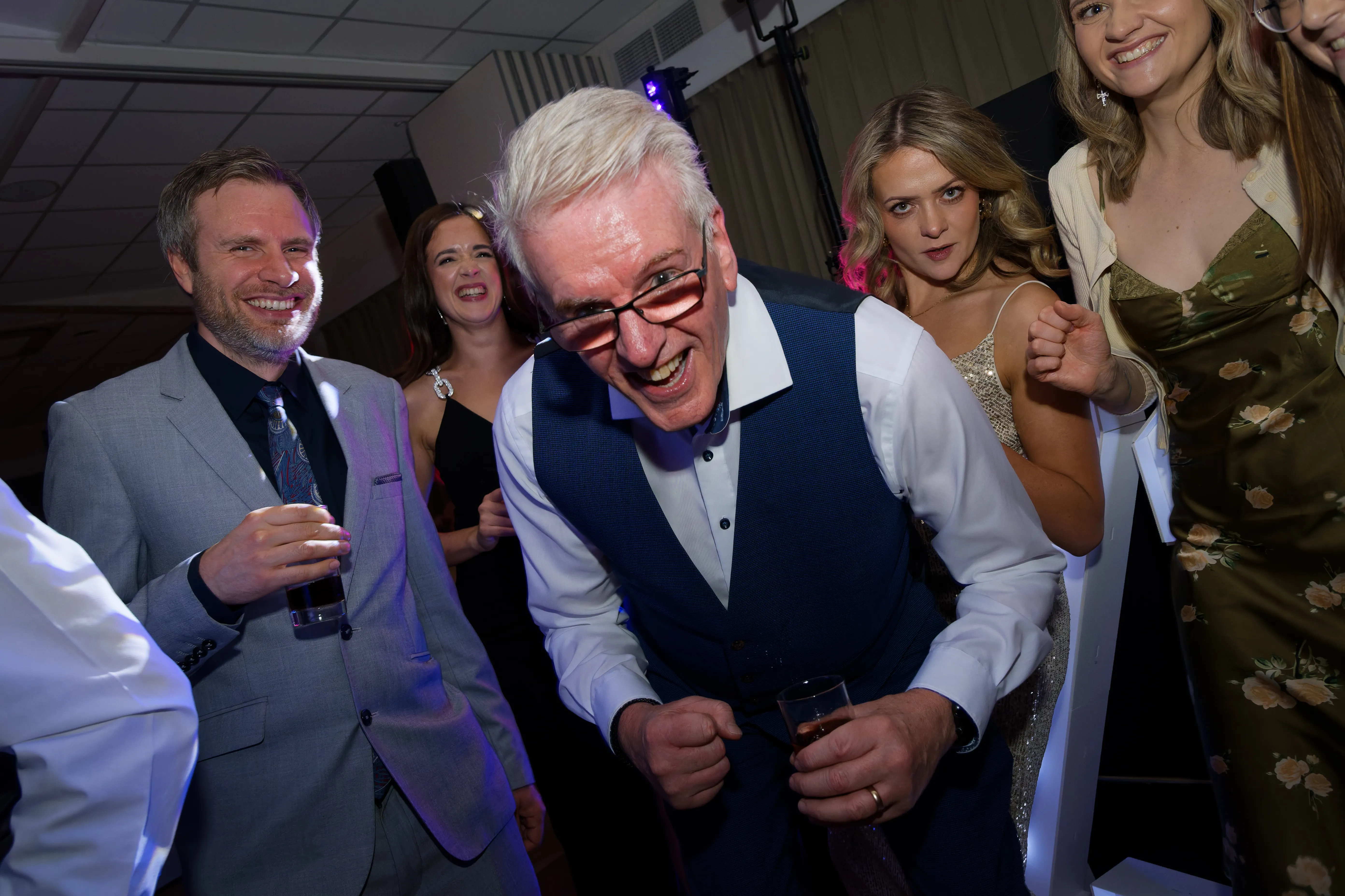 An older guest in glasses leaning towards the camera with a grin.