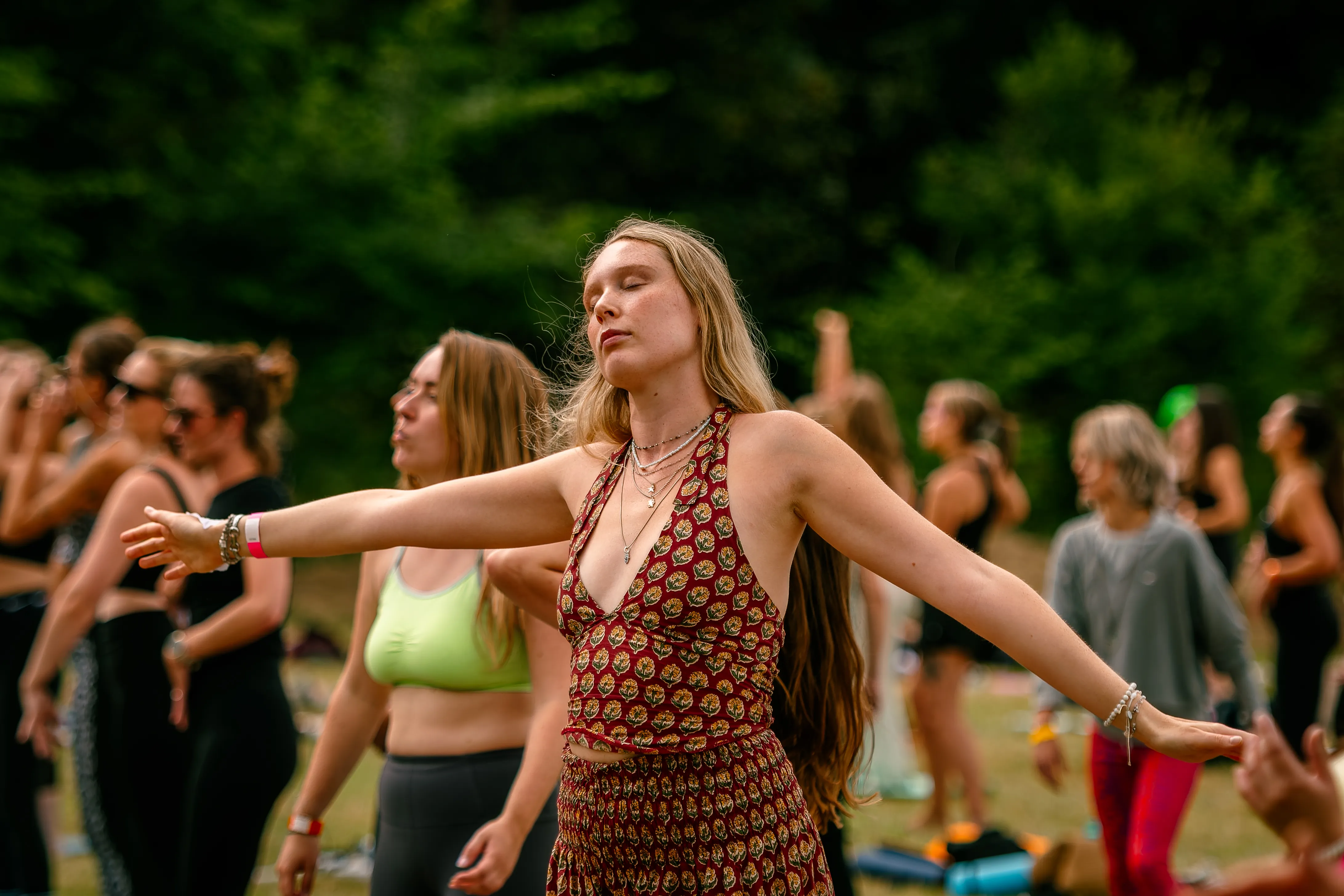 A young woman in a patterned halterneck dancing with her eyes closed and arms spread wide.