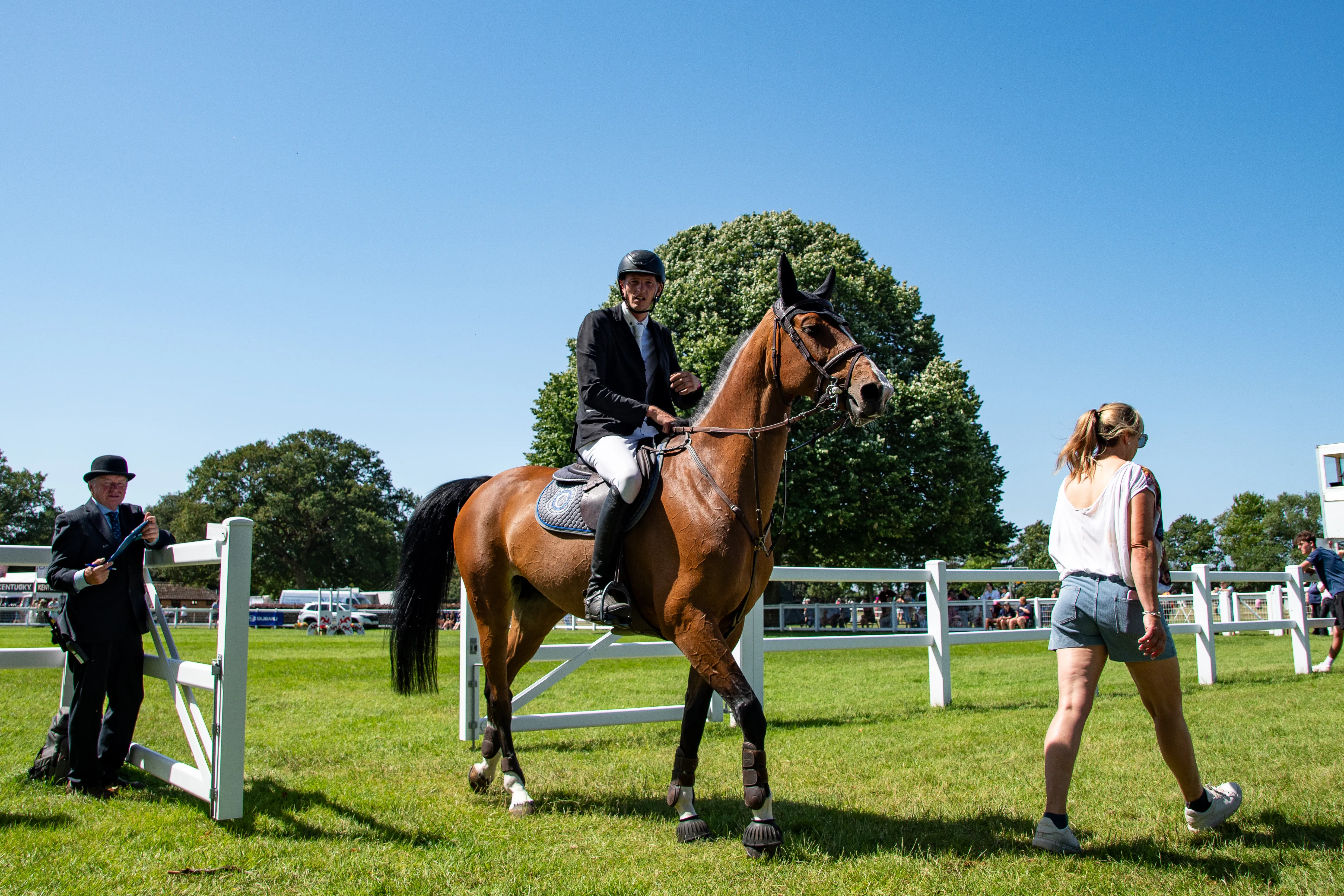 A horse and rider passing the practice fence as a steward crosses the ring.
