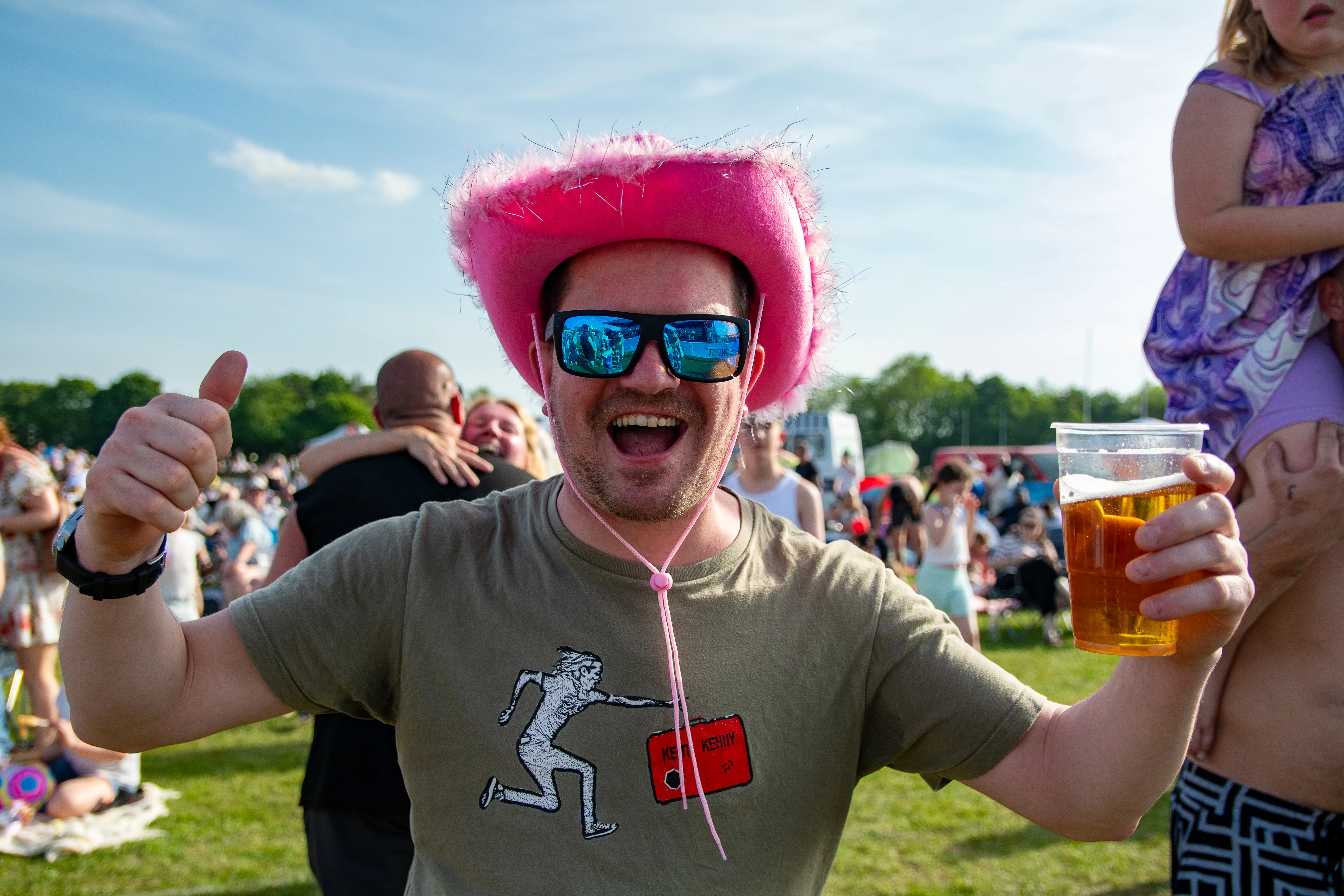 A man in a pink cowboy hat and sunglasses grinning with two pints.