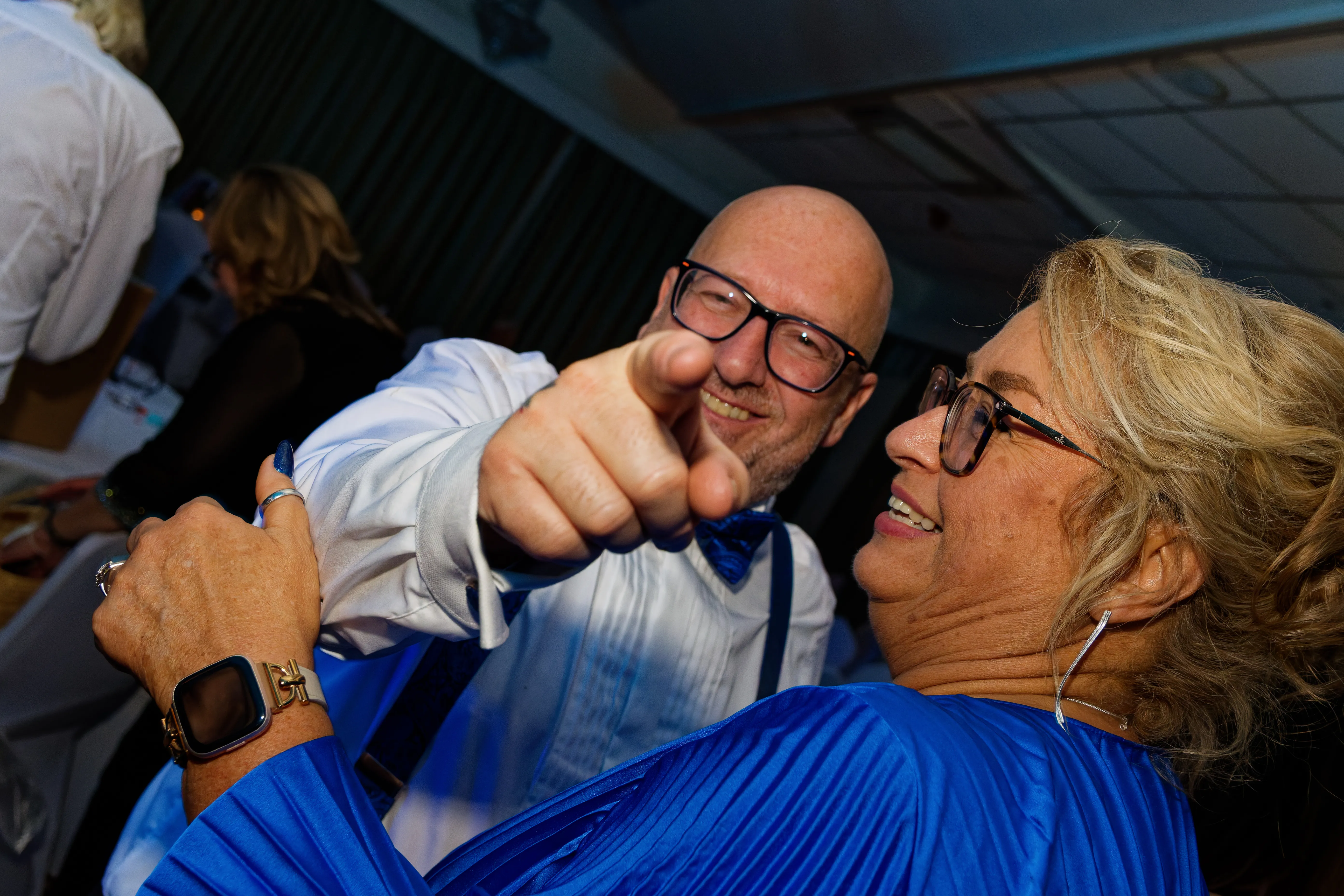 A man pointing to the camera while dancing with a friend in blue.
