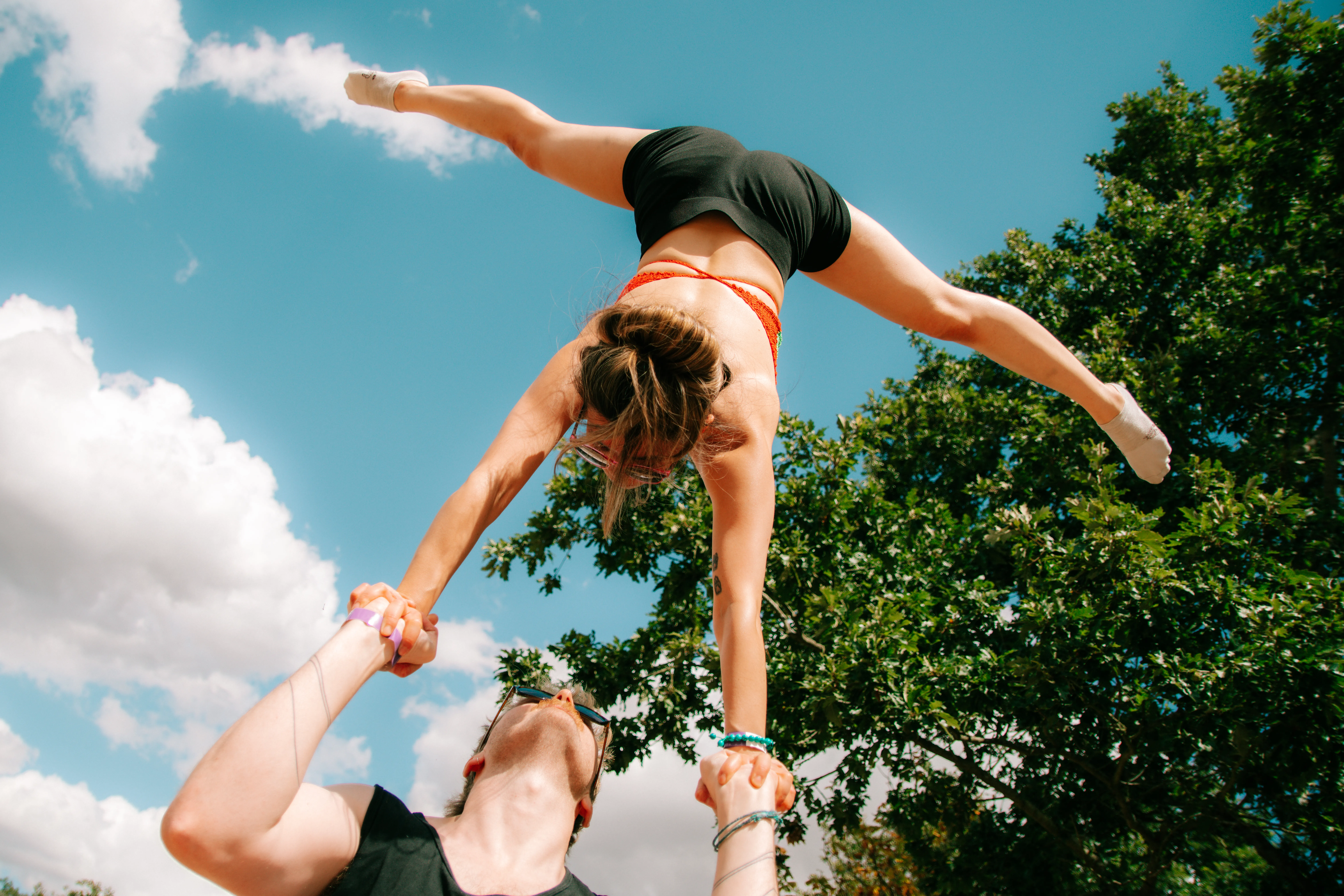 An acroyoga flyer balanced high above her base, arms and legs outstretched against a blue sky.
