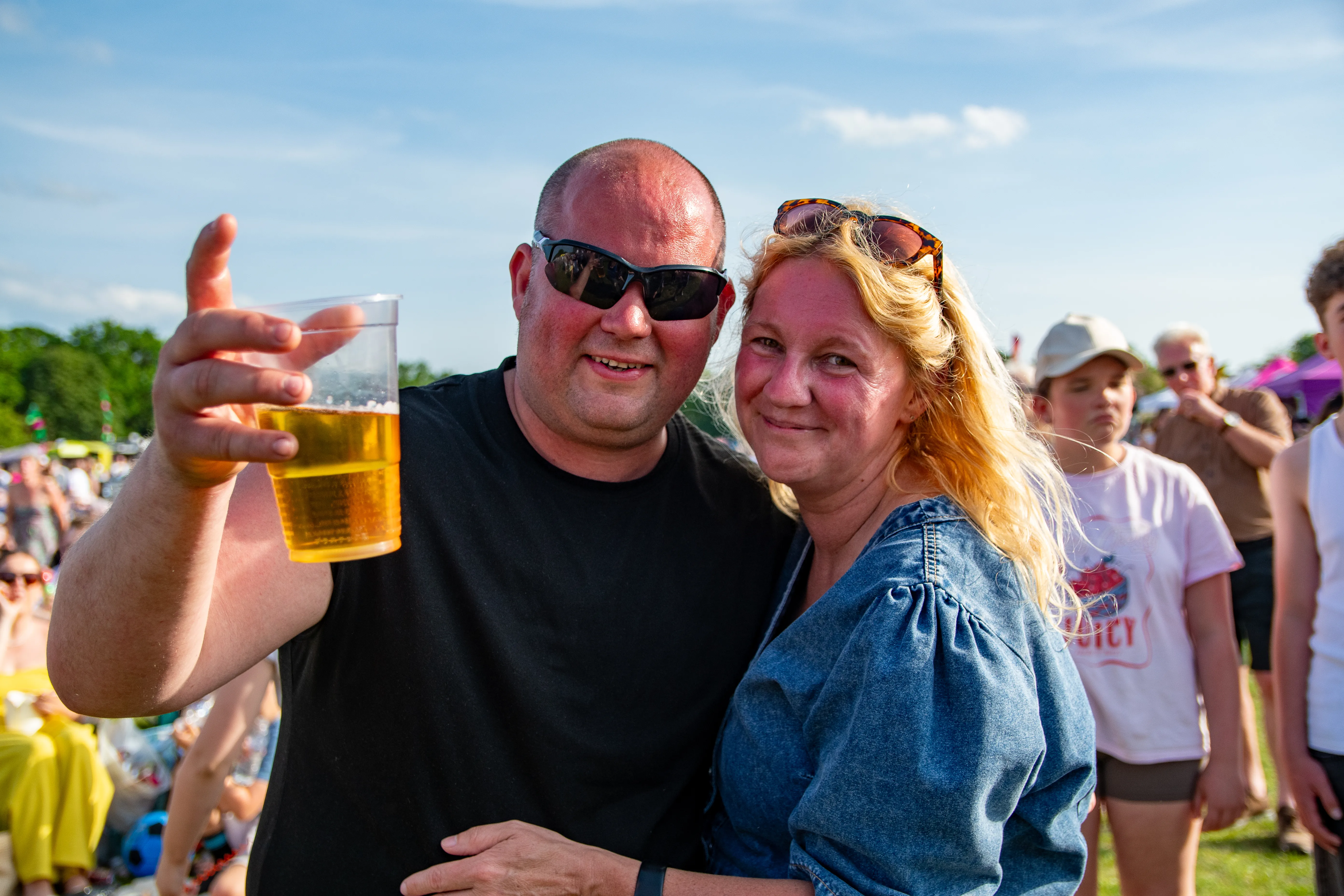 A couple in sunglasses raising a pint to the camera.
