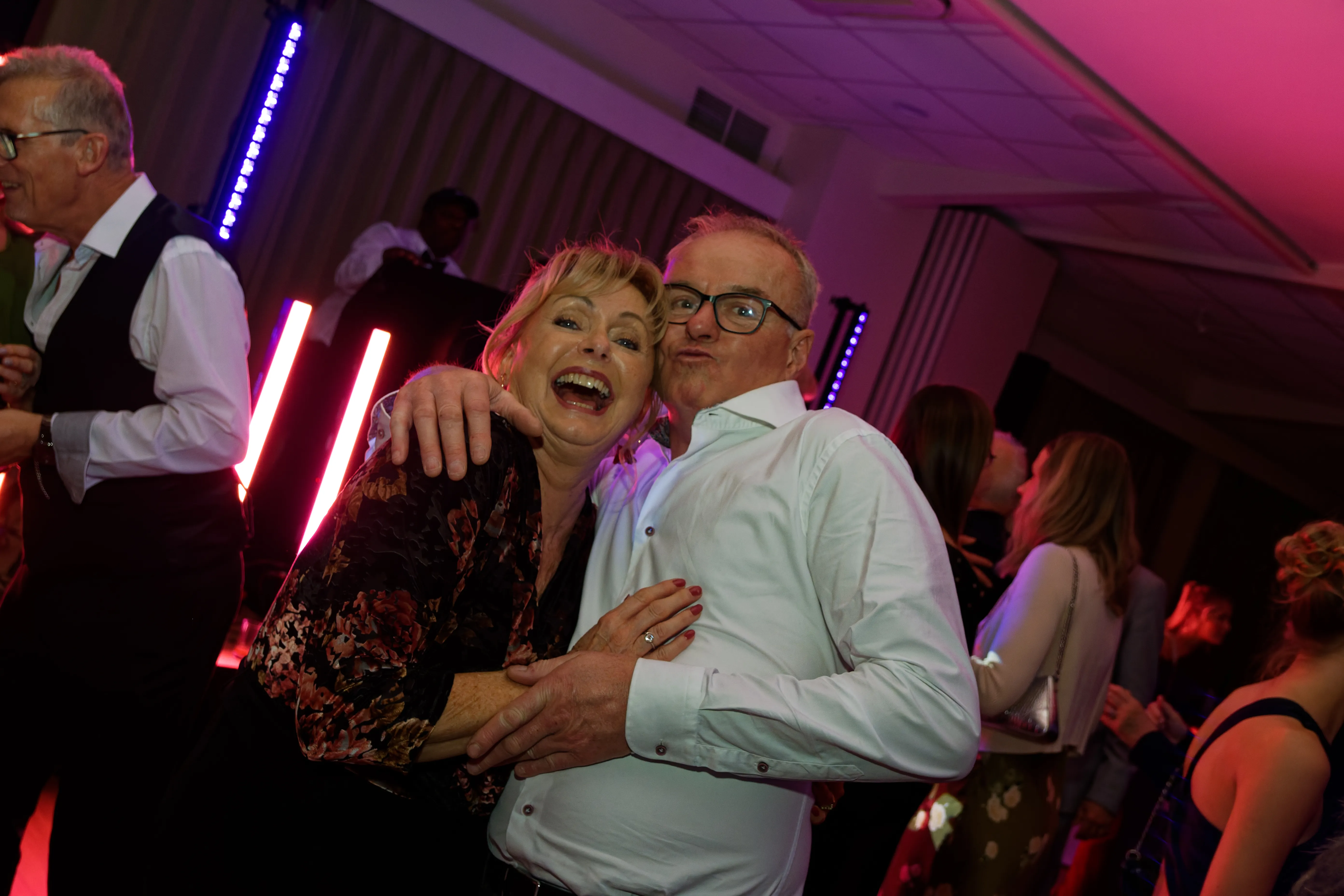 A couple laughing together as they dance in pink light.