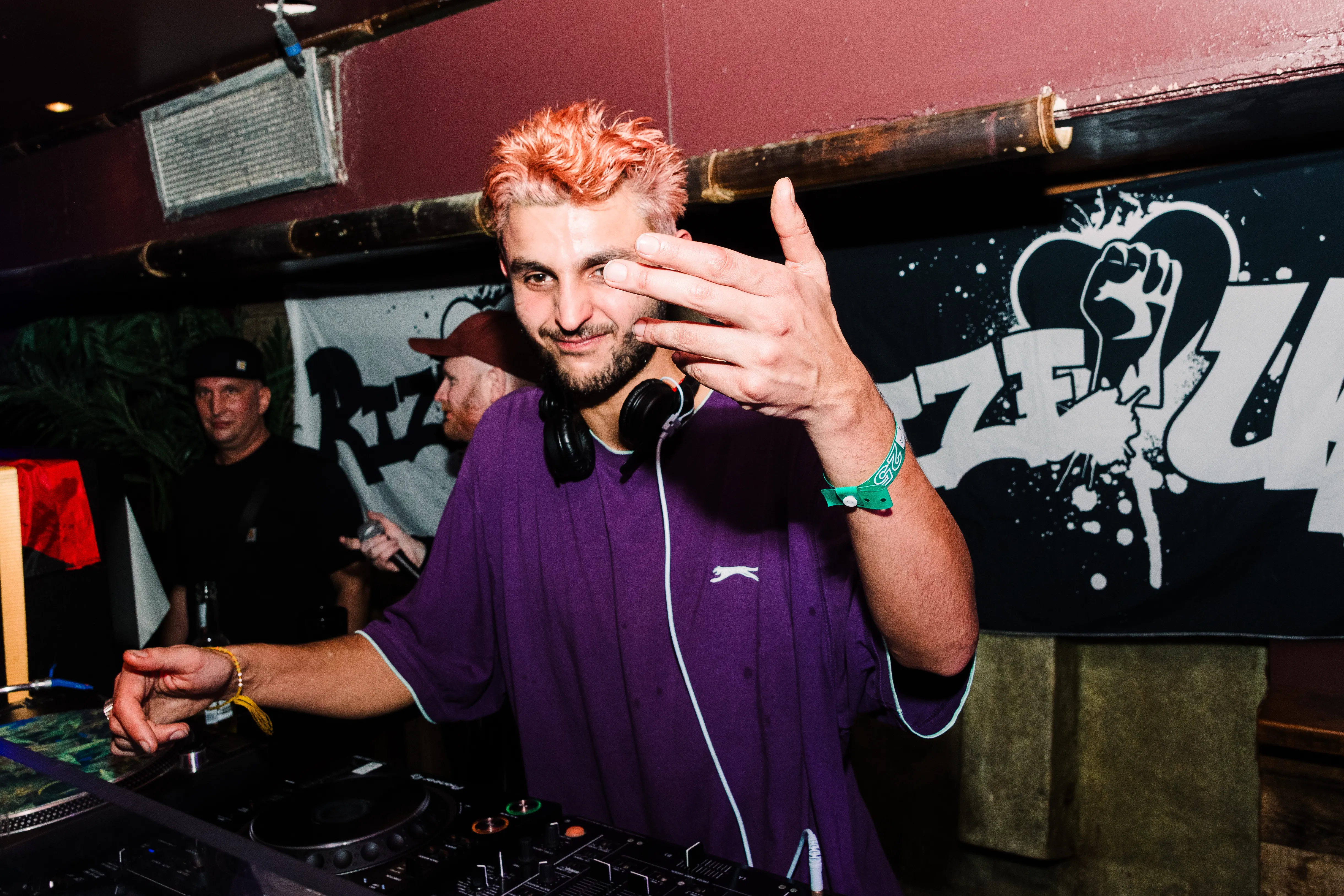 The DJ pointing to the camera mid-set, headphones round his neck.