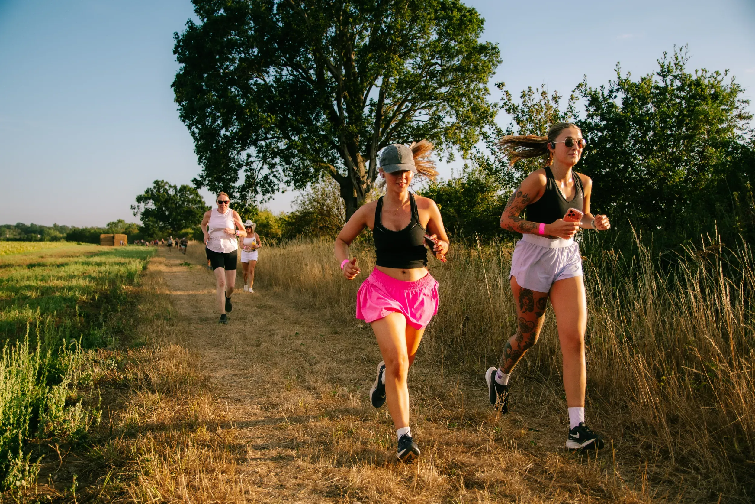 Two runners in the golden hour on a dry field path, the rest of the group strung out behind them.