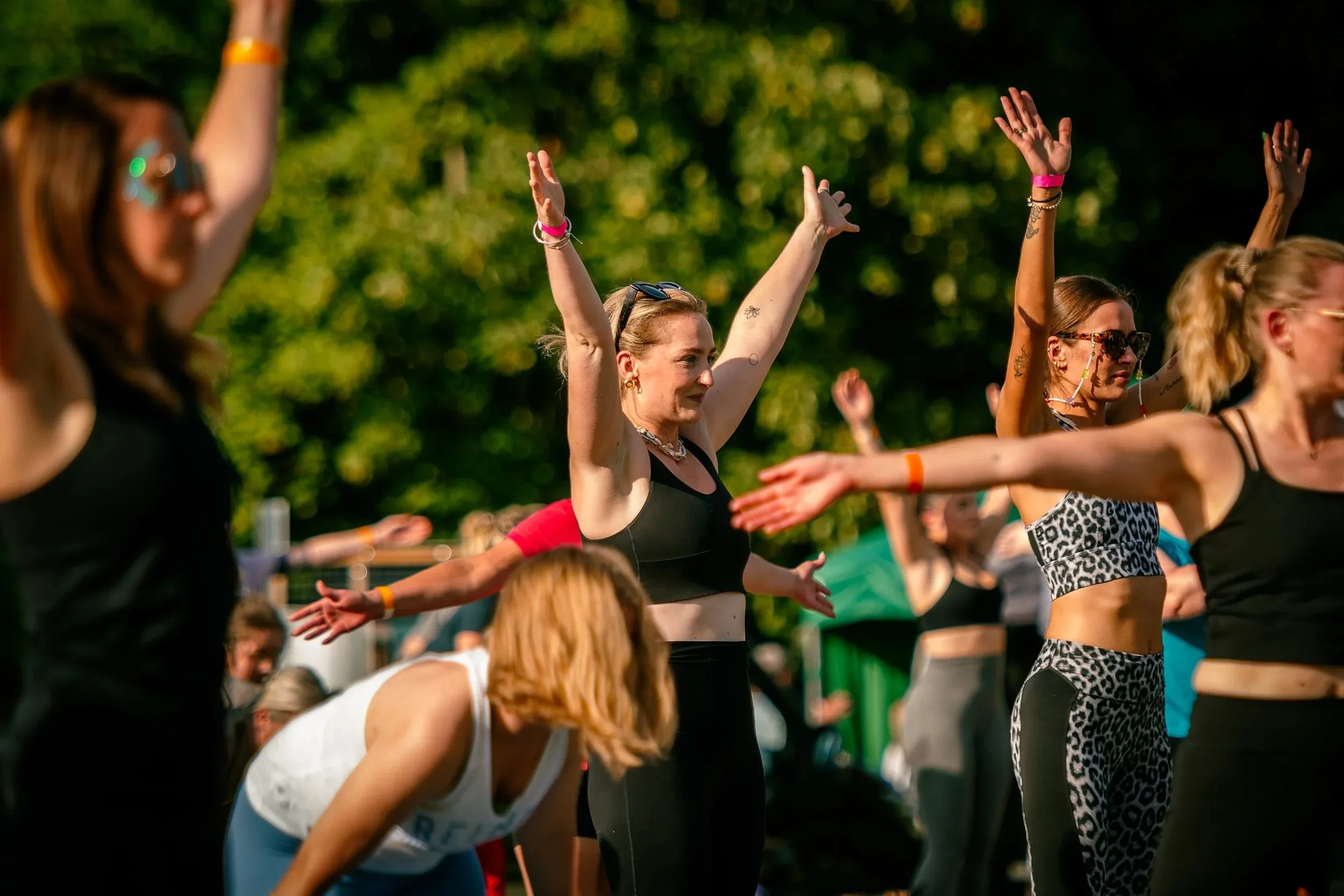 People with their arms raised mid-flow during an outdoor movement class in the sun.