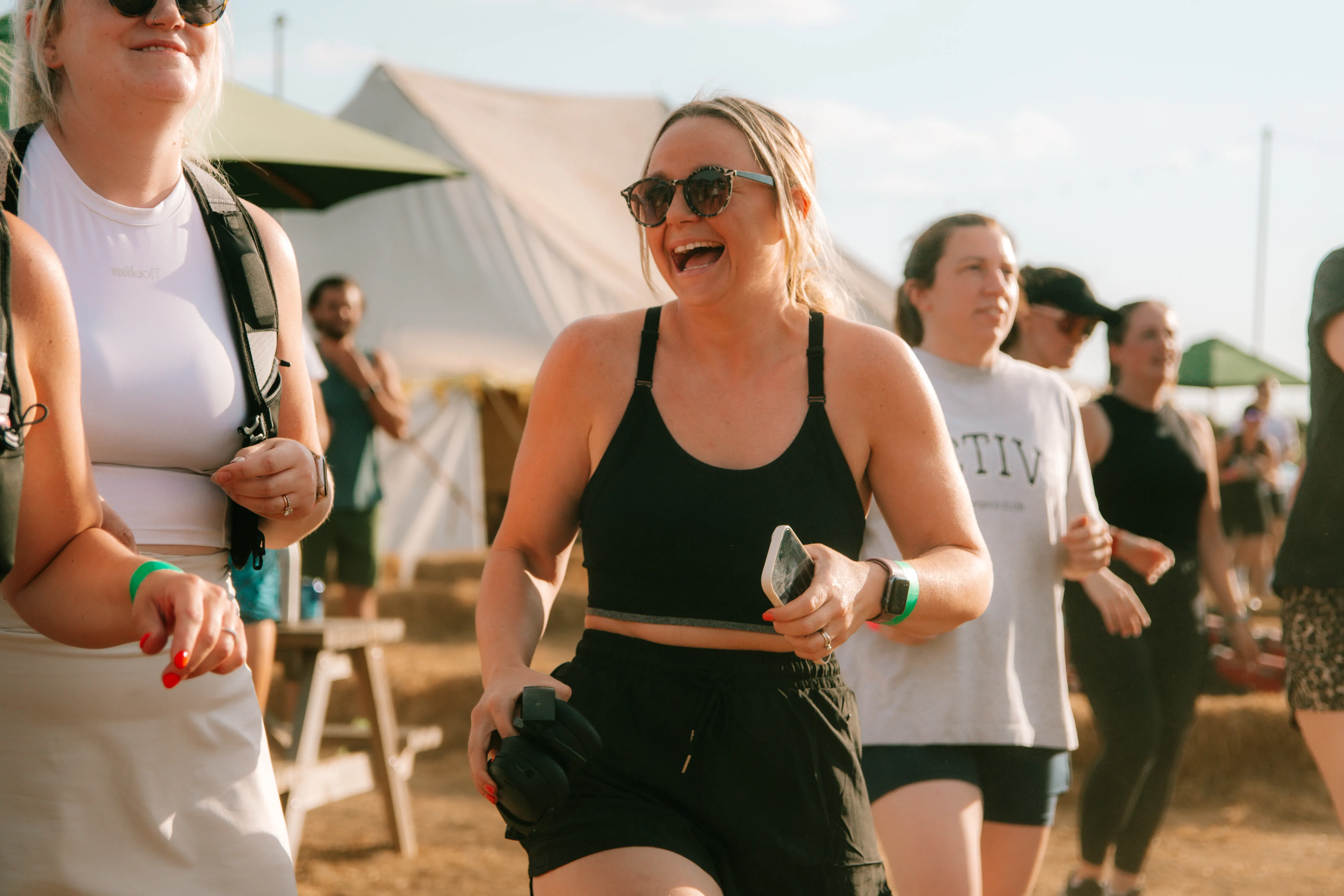 A runner laughing with her friends after the run, tents and hay bales behind them.