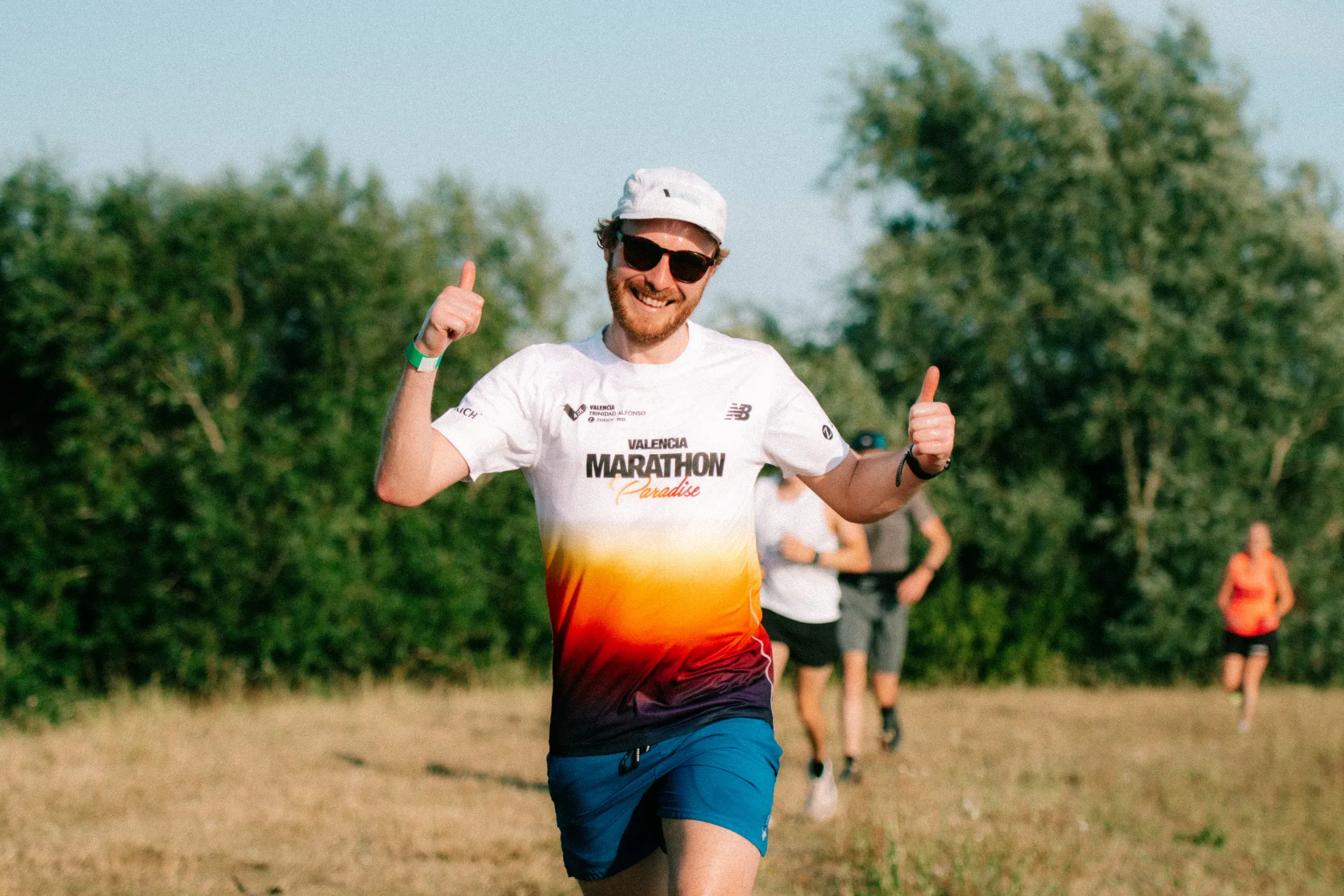A runner in a Valencia Marathon shirt and white cap giving two thumbs up as he comes up the field.