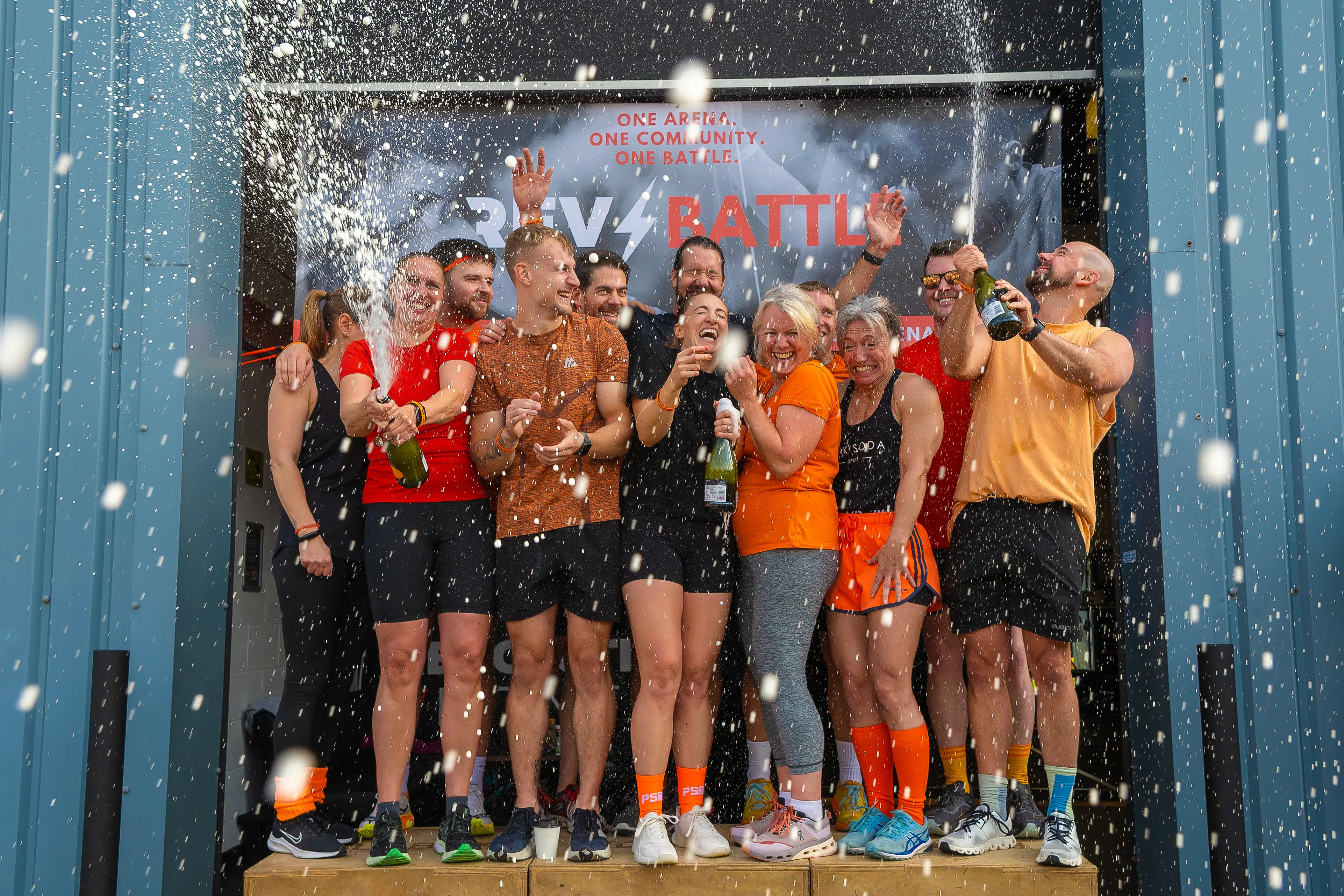 A team spraying champagne in celebration on a podium after a fitness competition.