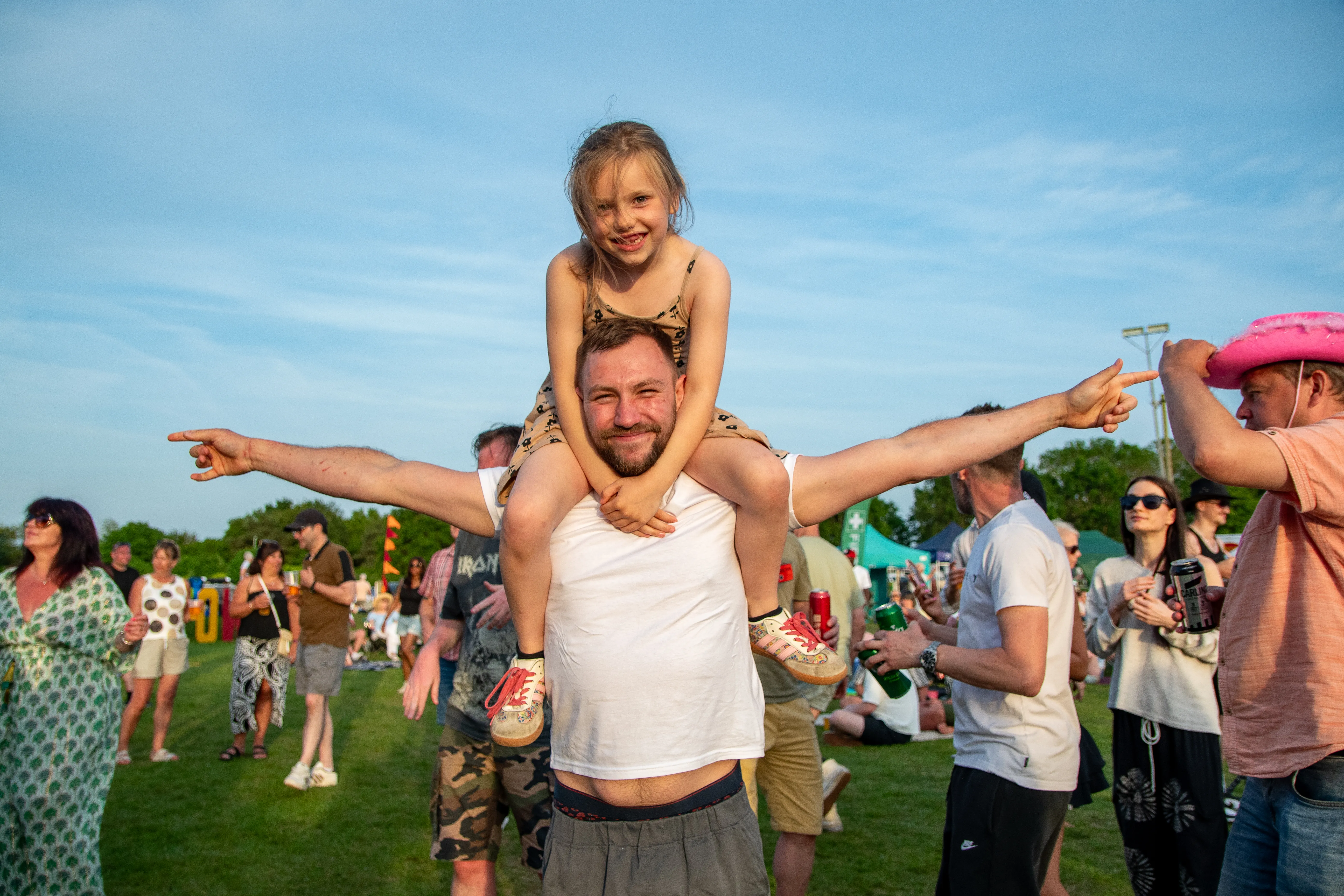 A girl riding on her dad's shoulders, both with arms spread wide.