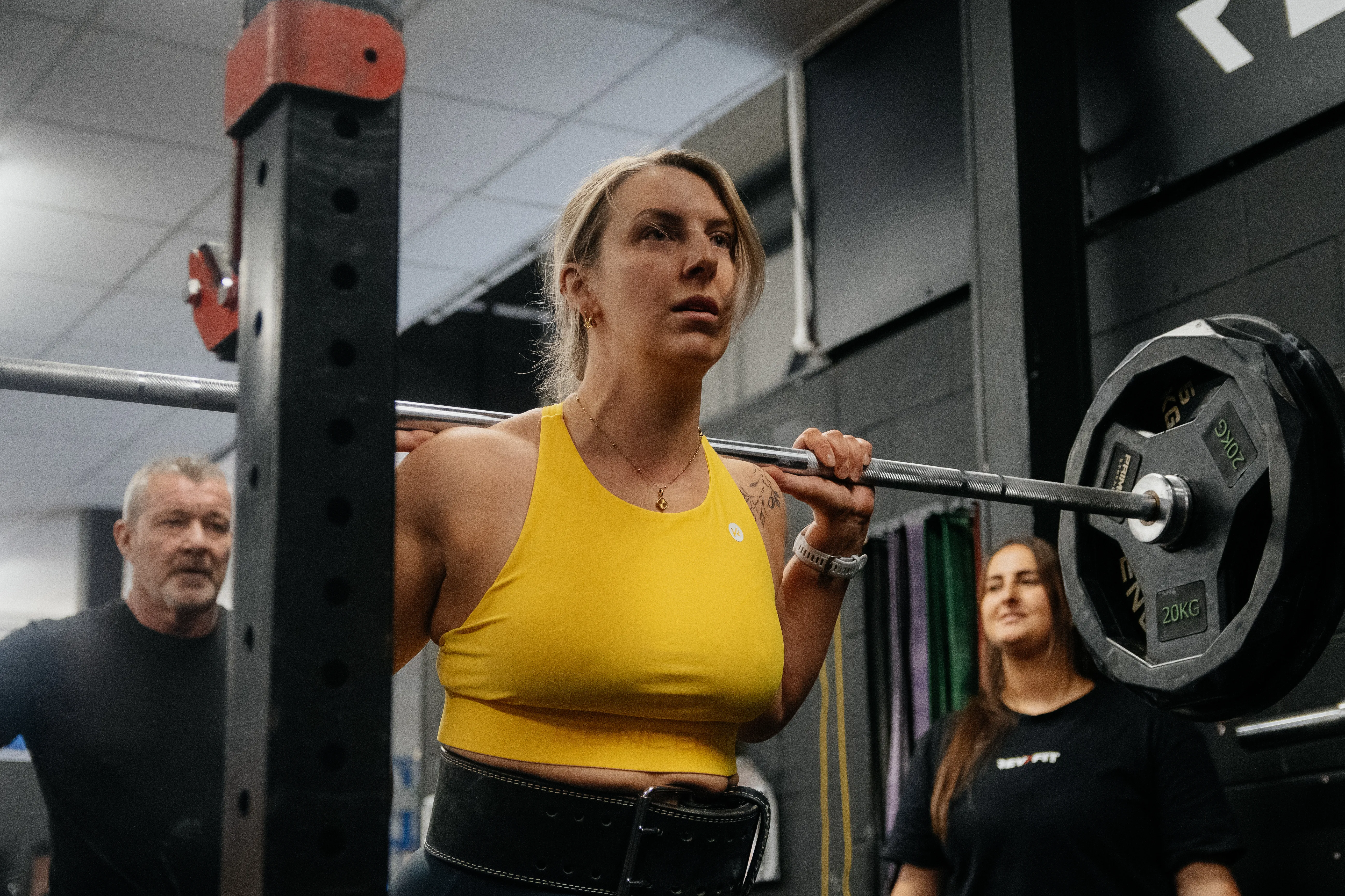 A competitor in a yellow vest stepping under the bar at the rack.