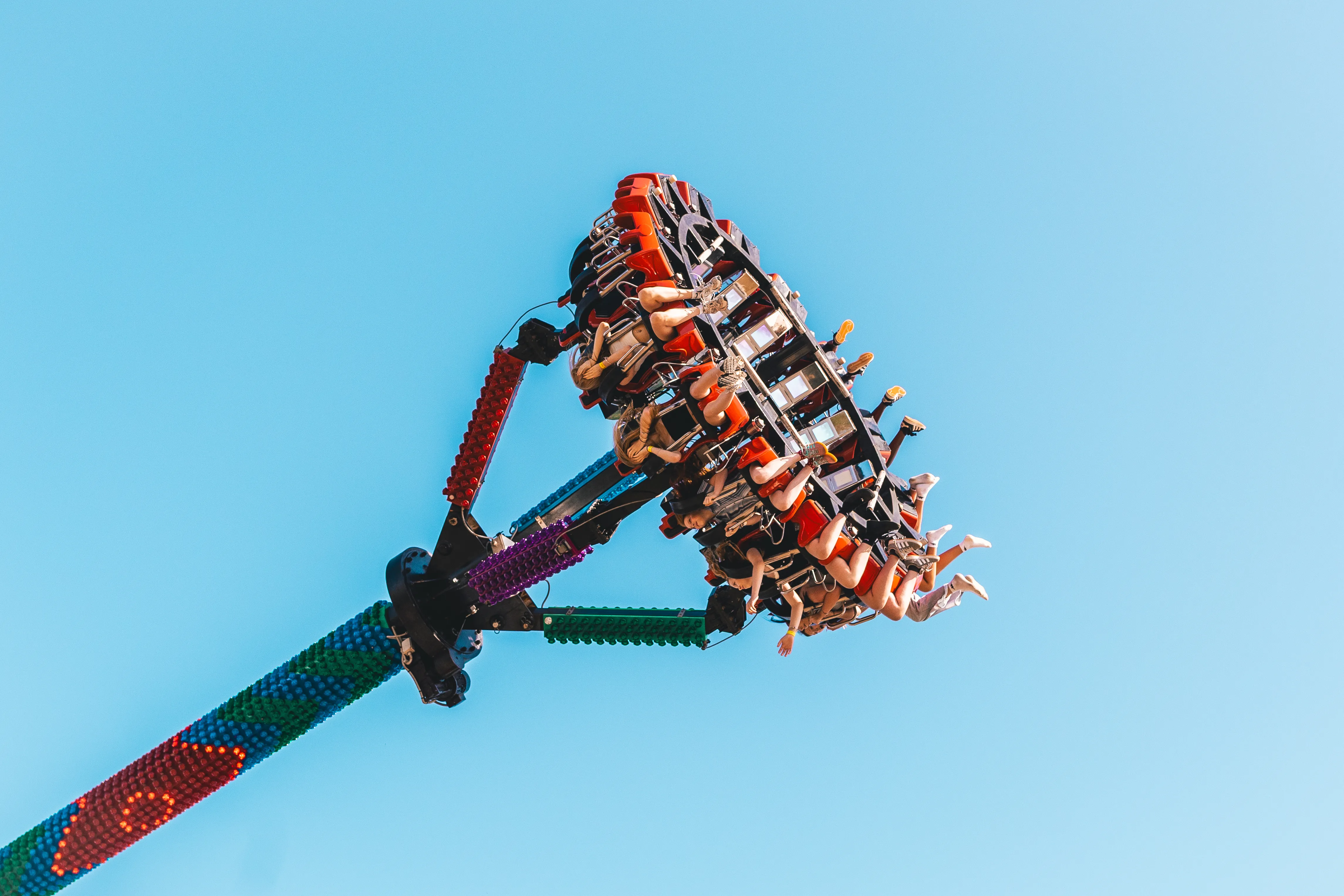 A fairground swing ride raised against a bright blue sky, riders strapped into its spinning arm.