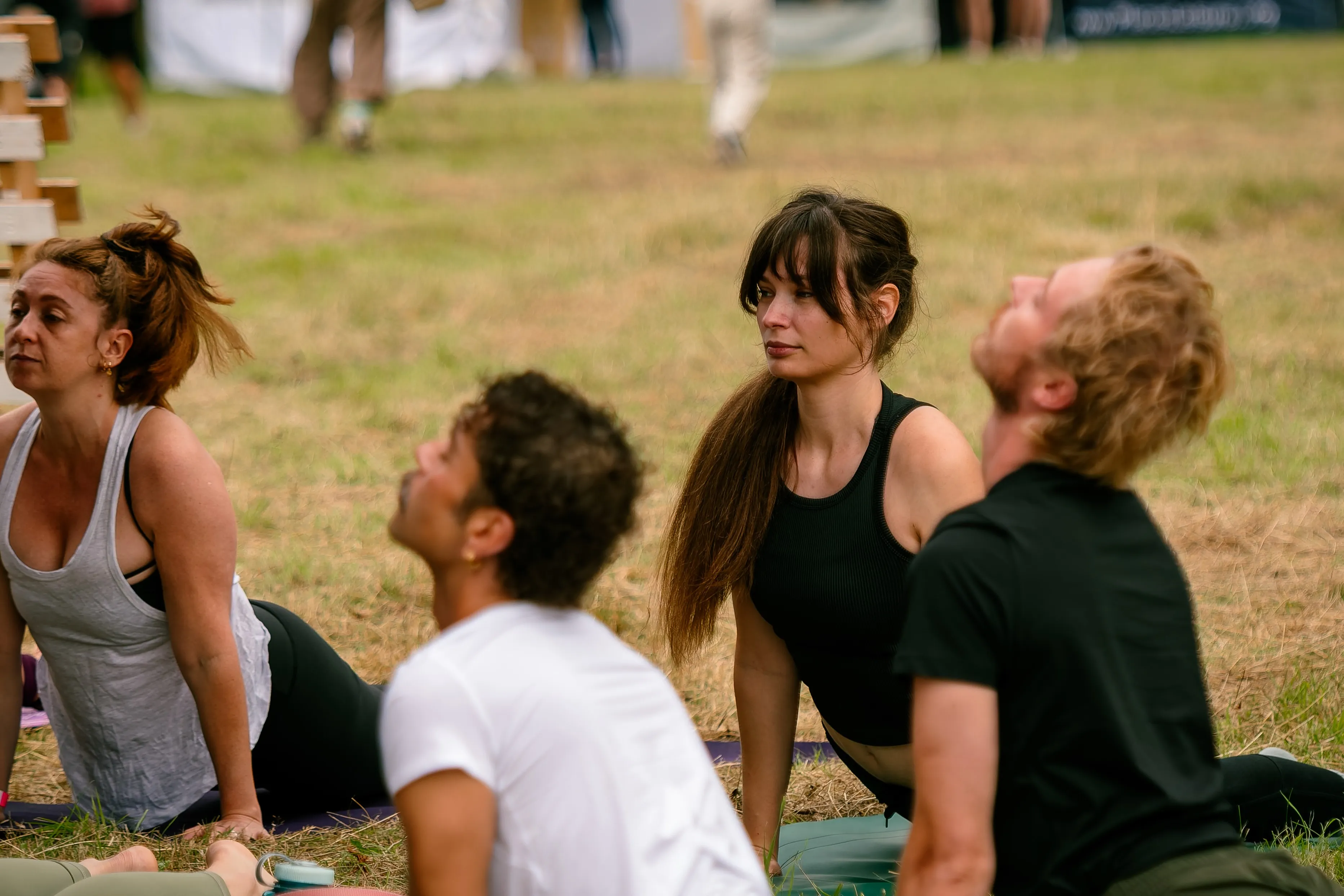 People sitting on yoga mats outdoors, one man laughing as he looks up.