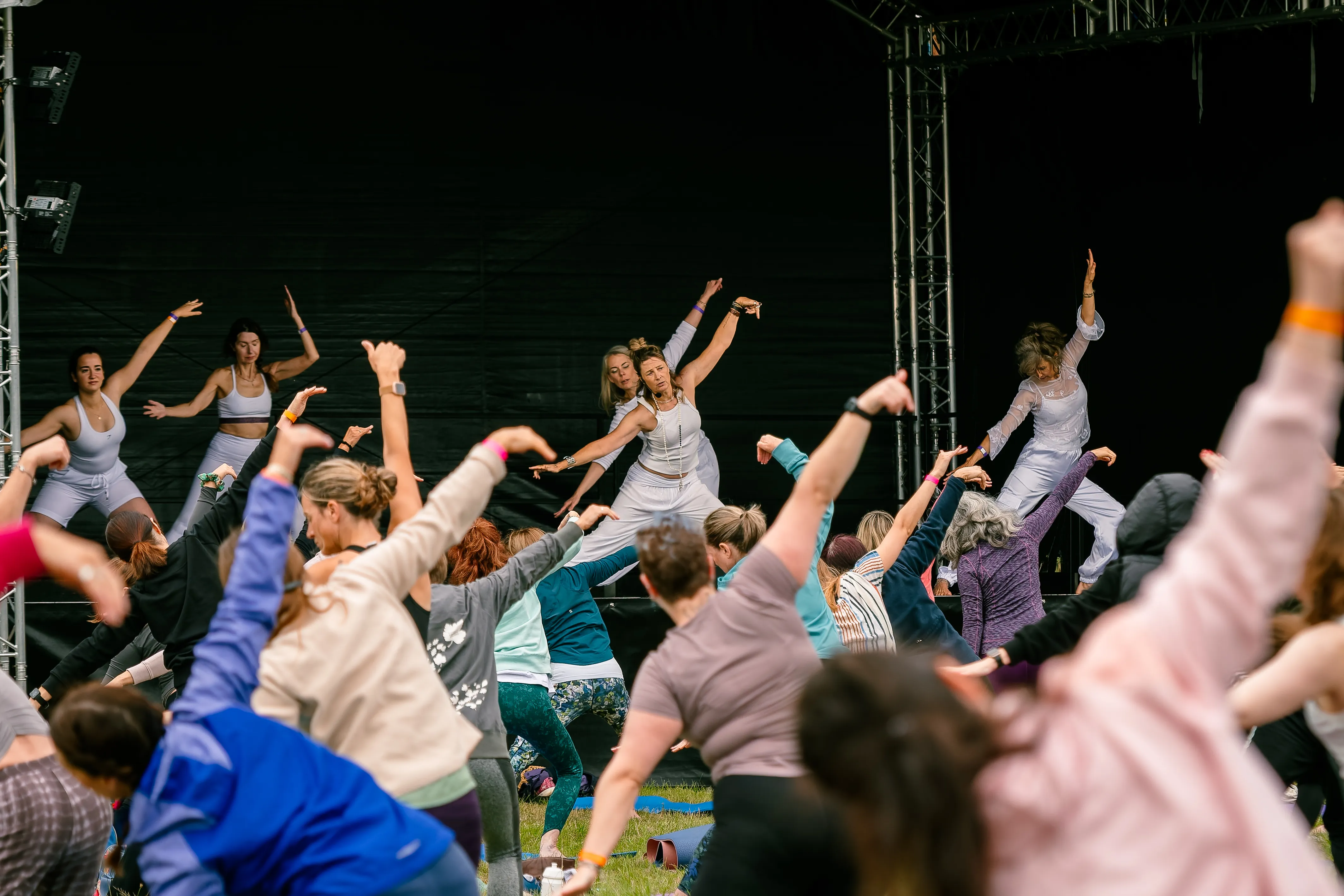 Instructors in white leading a flowing side-stretch from the stage, the whole crowd mirroring them.