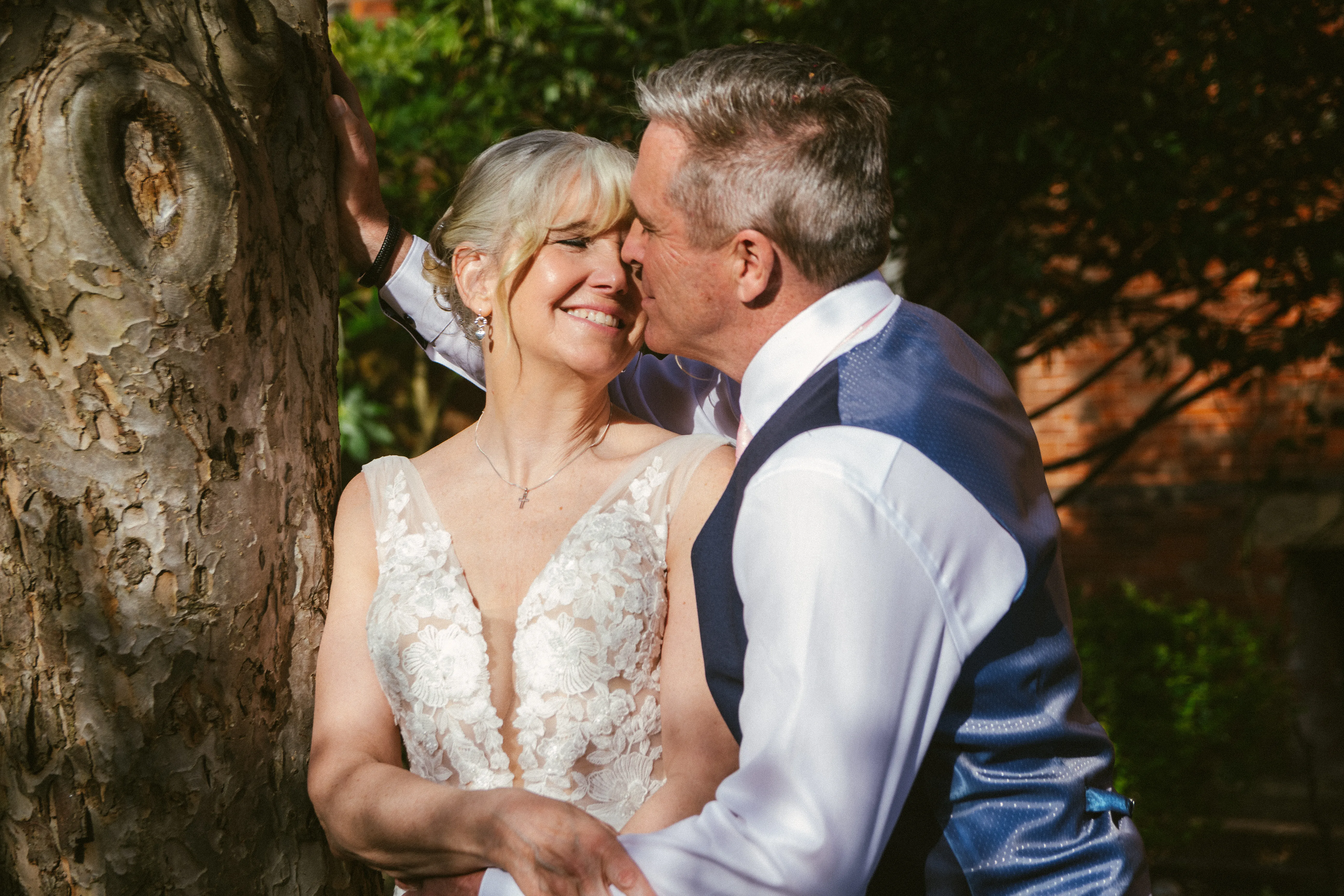A bride and groom leaning close beneath a tree, foreheads almost touching in soft light.