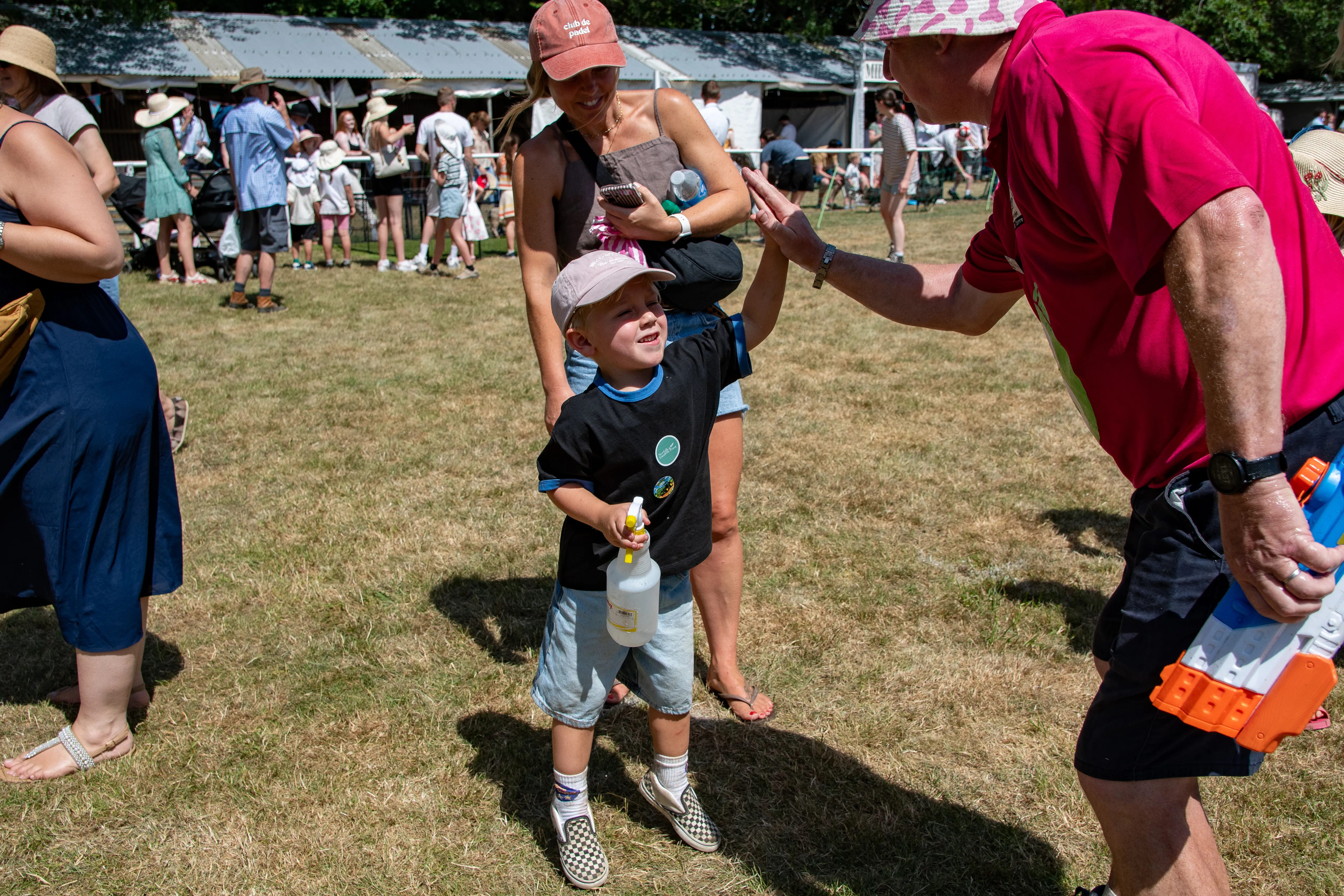 A small boy in a cap being greeted by family in the busy showground.